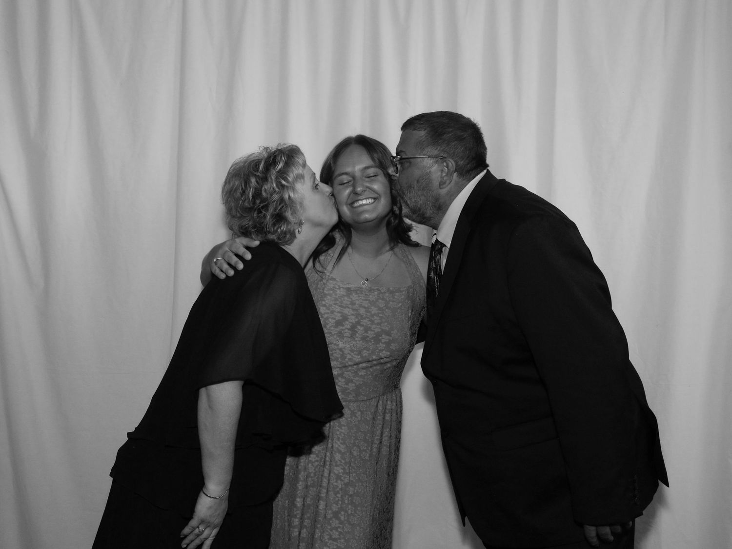 Black and white photo of a woman being kissed on both cheeks by an older couple at a formal event.