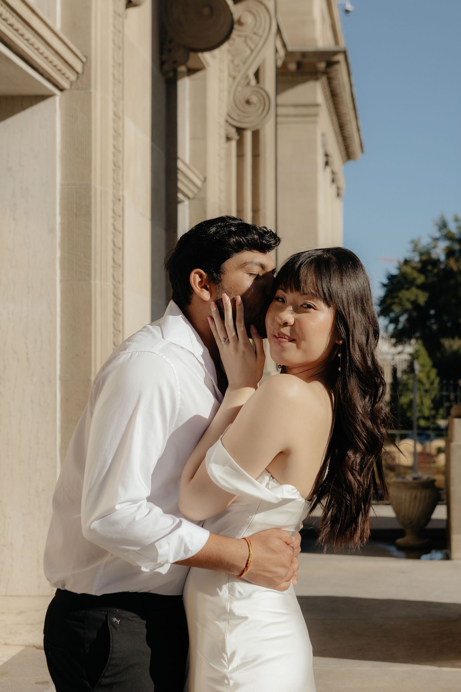 A couple shares an intimate moment against a classical architectural backdrop.