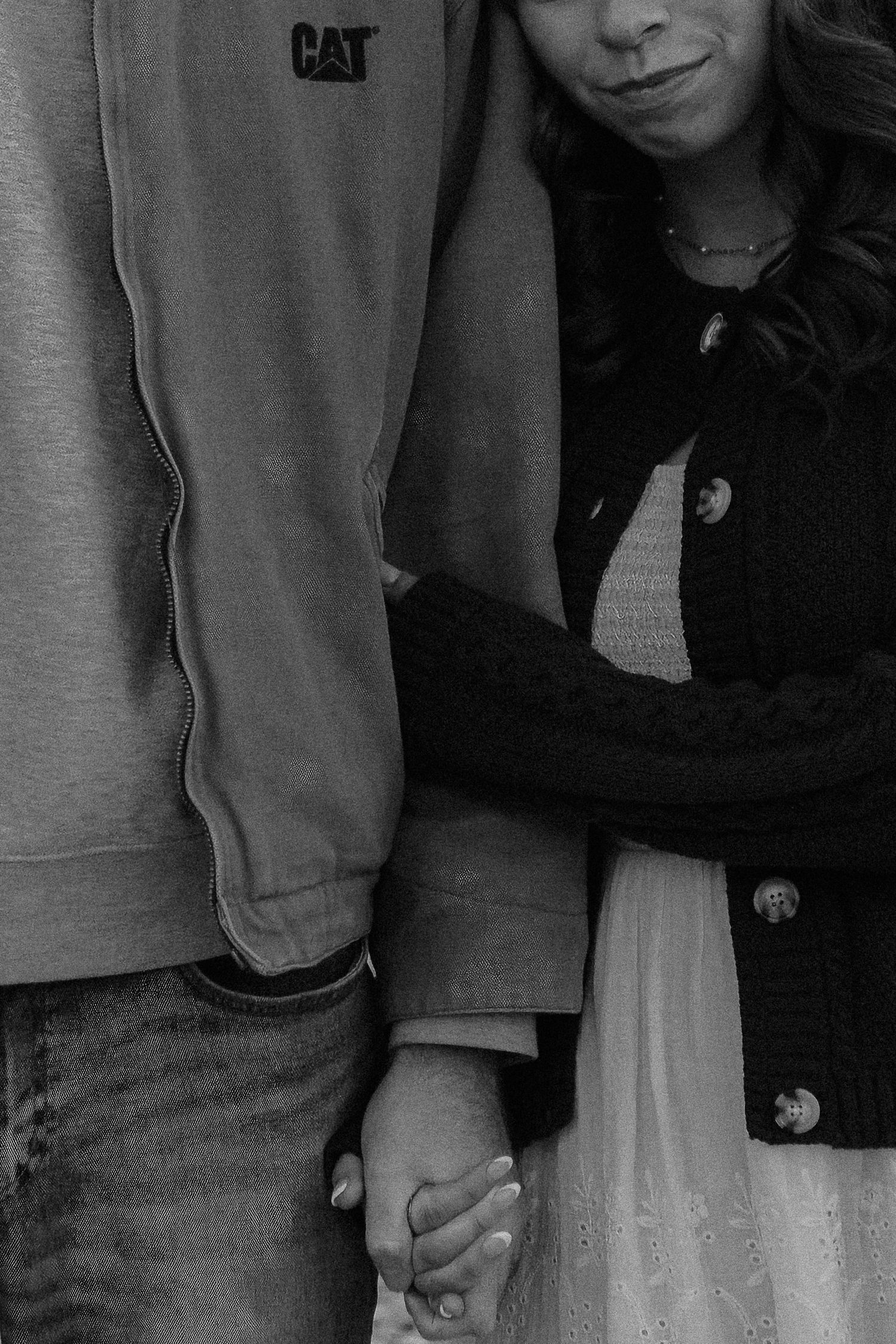 Close-up black and white photo showing couple holding hands while wearing casual attire.