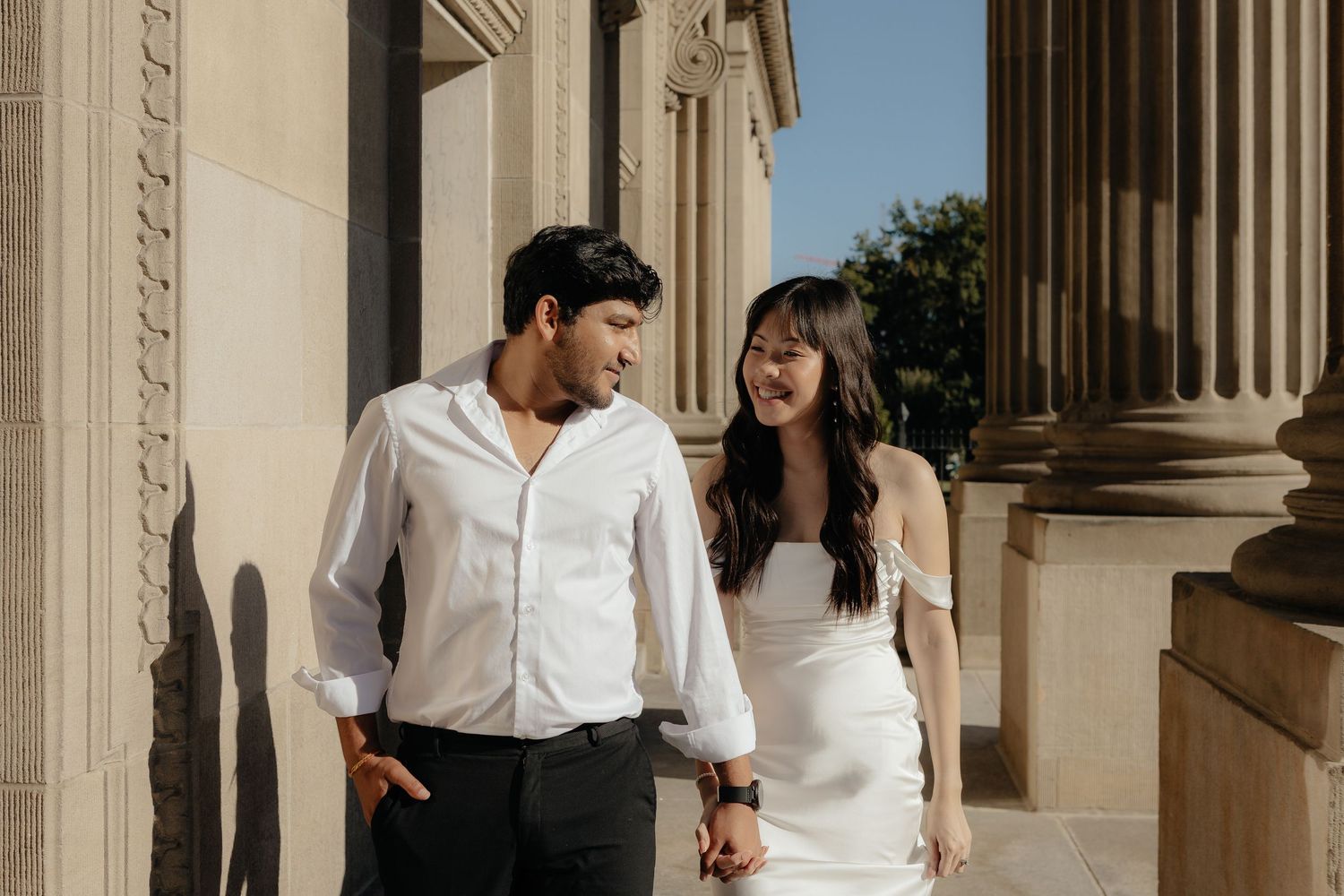 Couple shares an intimate moment in an elegant columned hallway with white architecture.