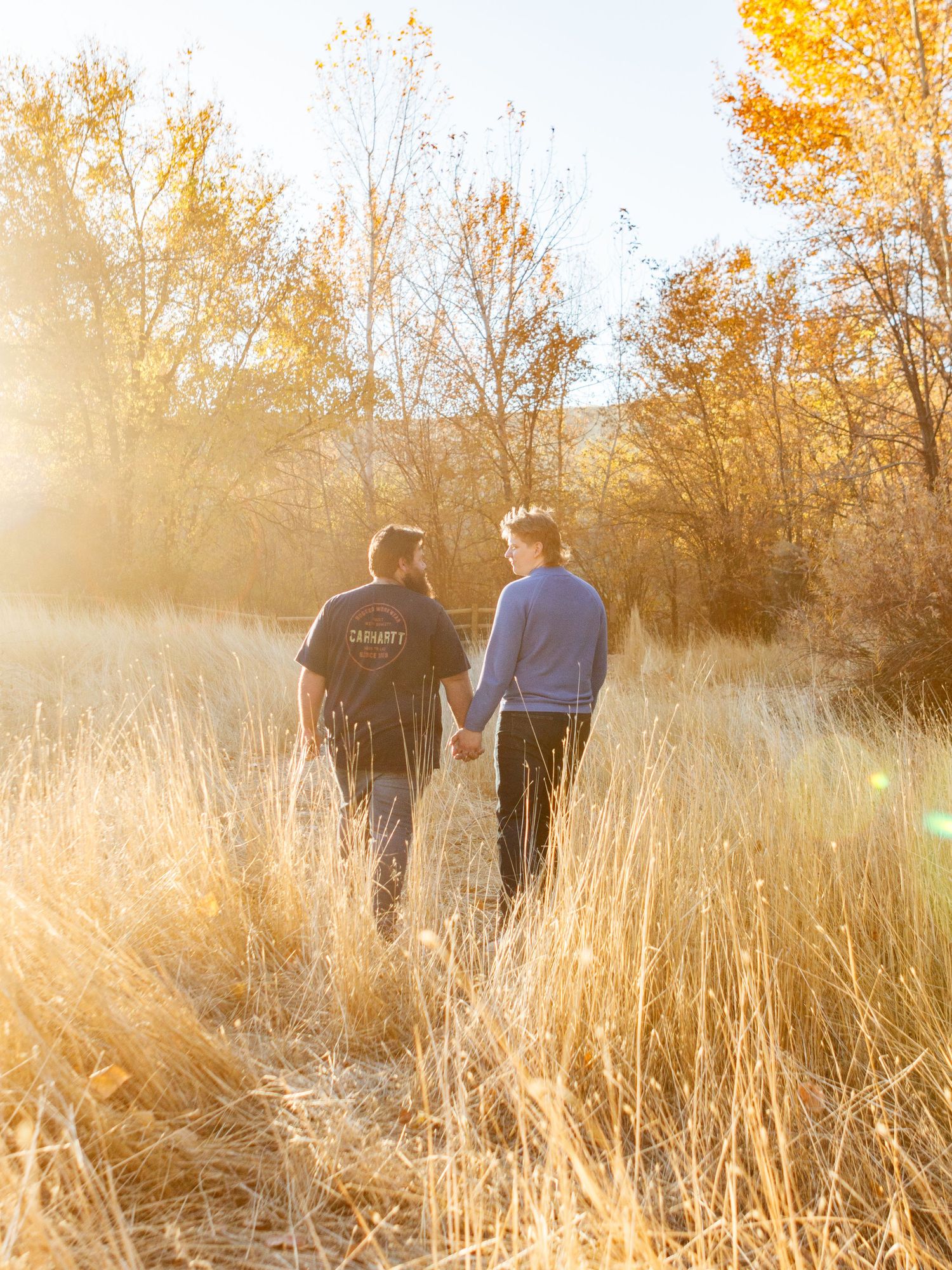 A couple walks together through golden autumn grasses at sunset with warm backlighting creating a dreamy atmosphere.