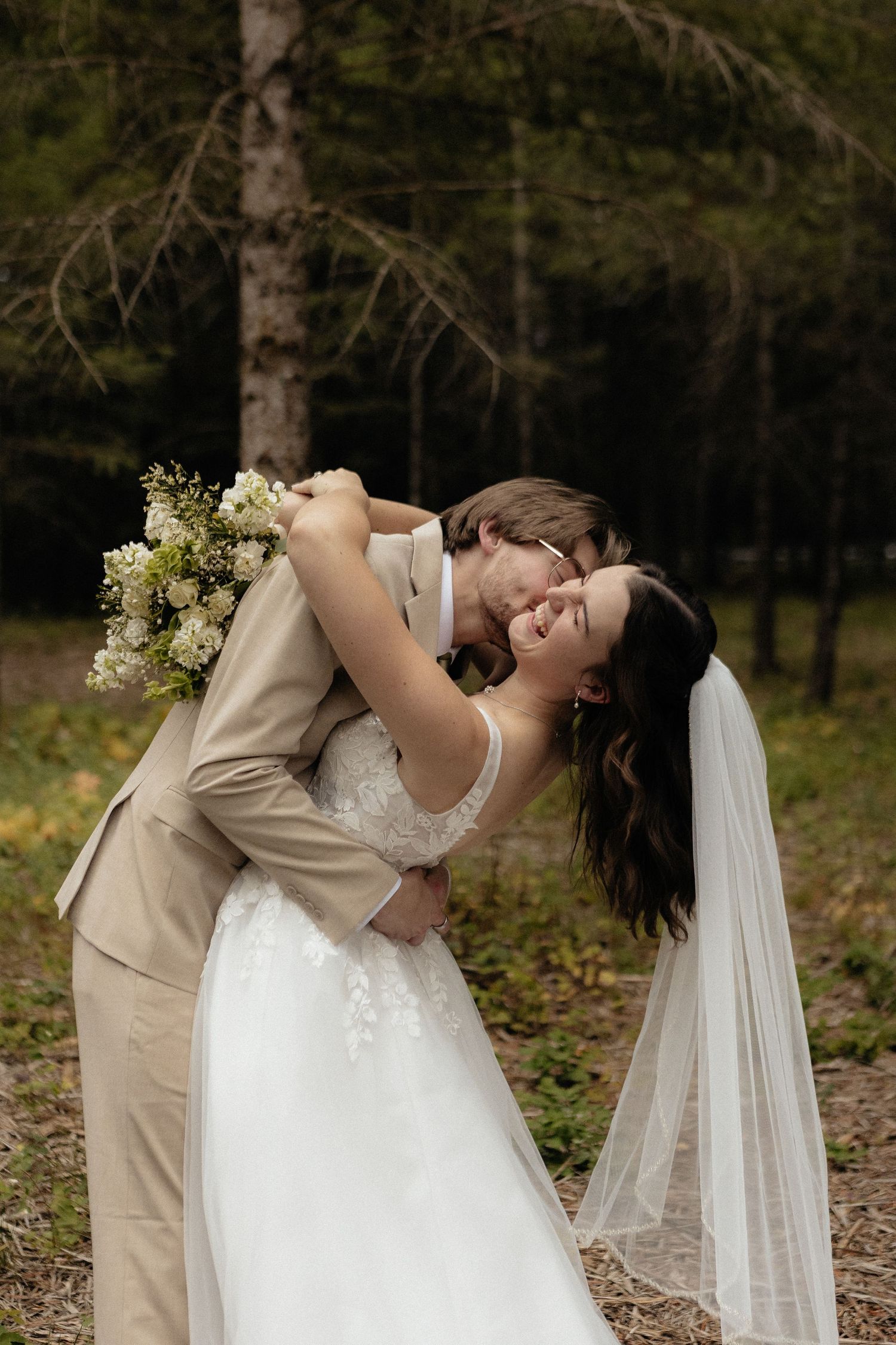A romantic wedding moment captured in a forest setting with soft natural lighting.