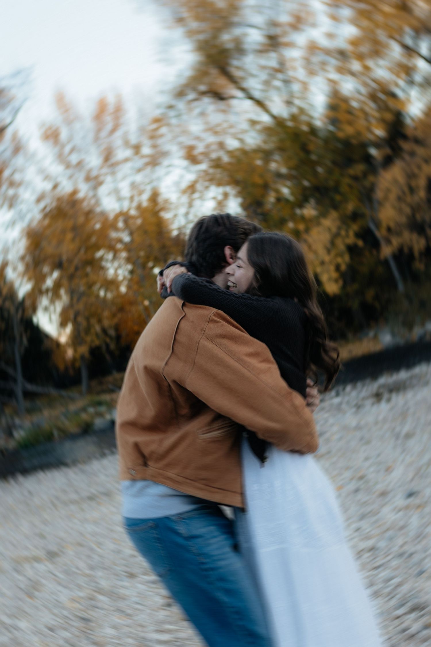 Intimate embrace captured in motion with autumn trees blurred in the background.