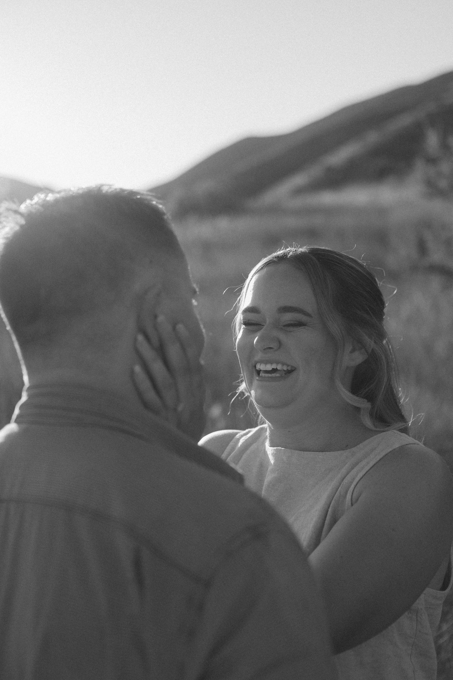 A joyful moment captured in black and white as a couple shares laughter in an outdoor setting.