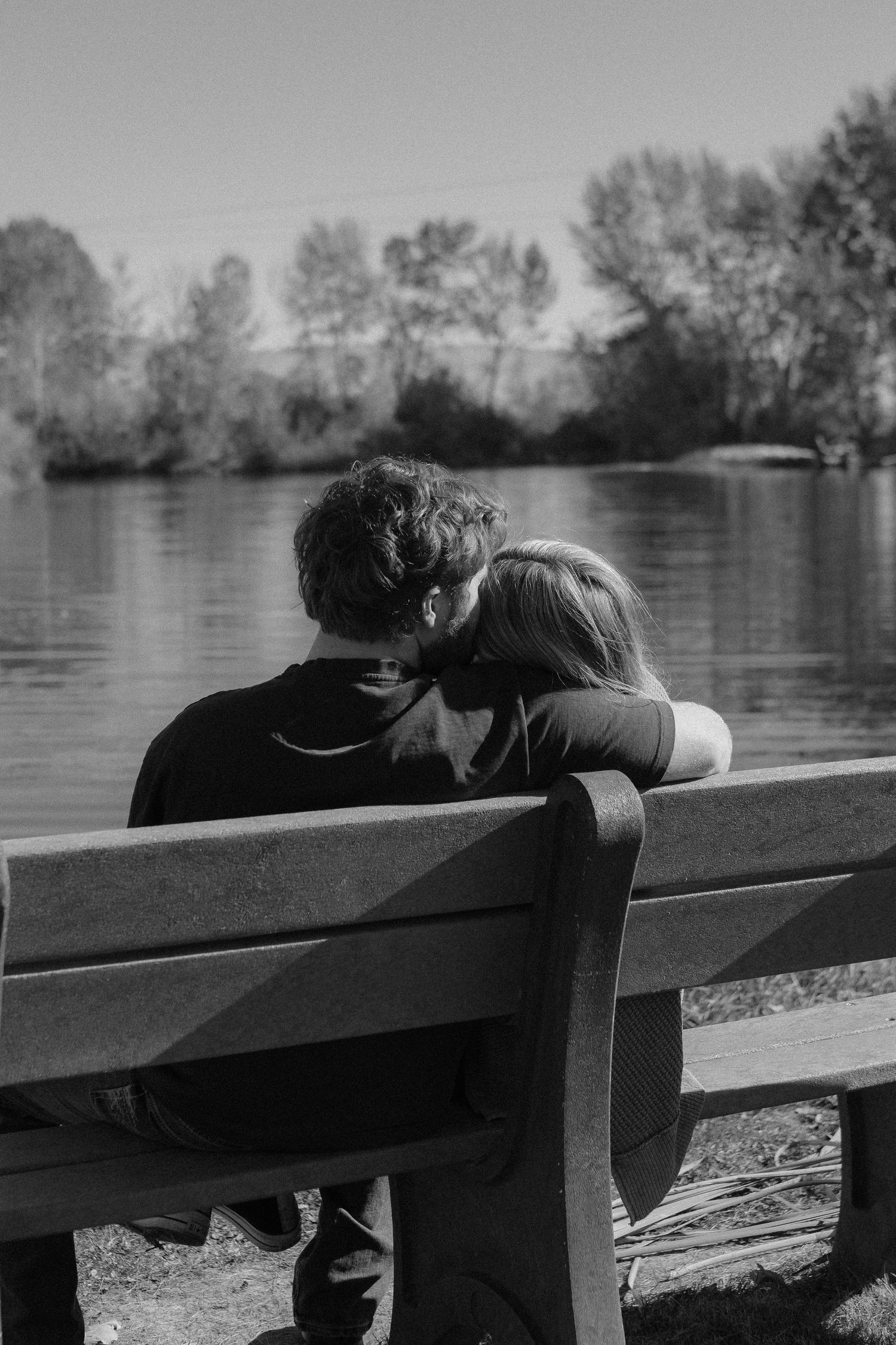 A couple sits together on a park bench overlooking a serene lake.