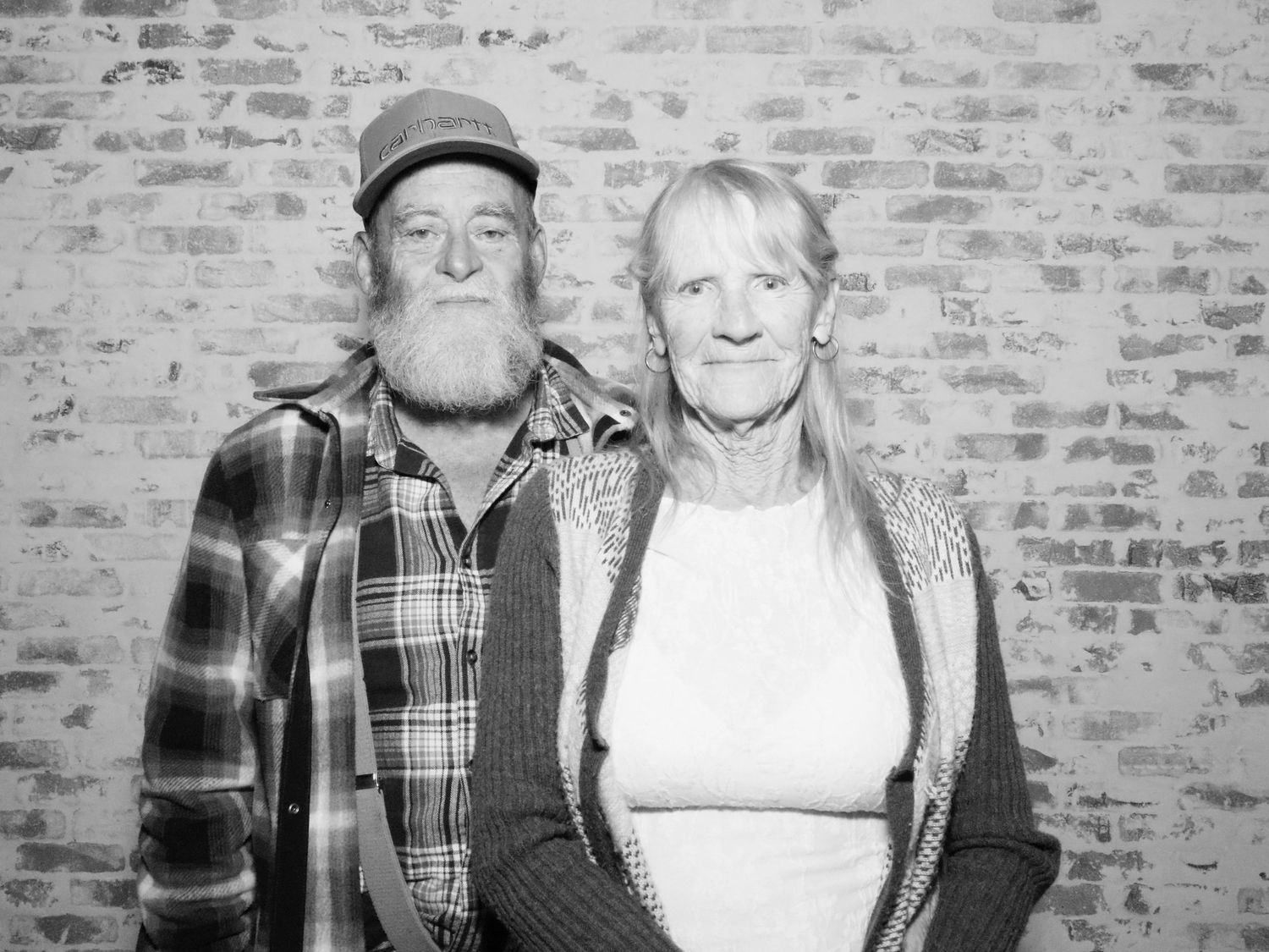 Casual portrait of people in plaid and casual wear against textured brick wall.