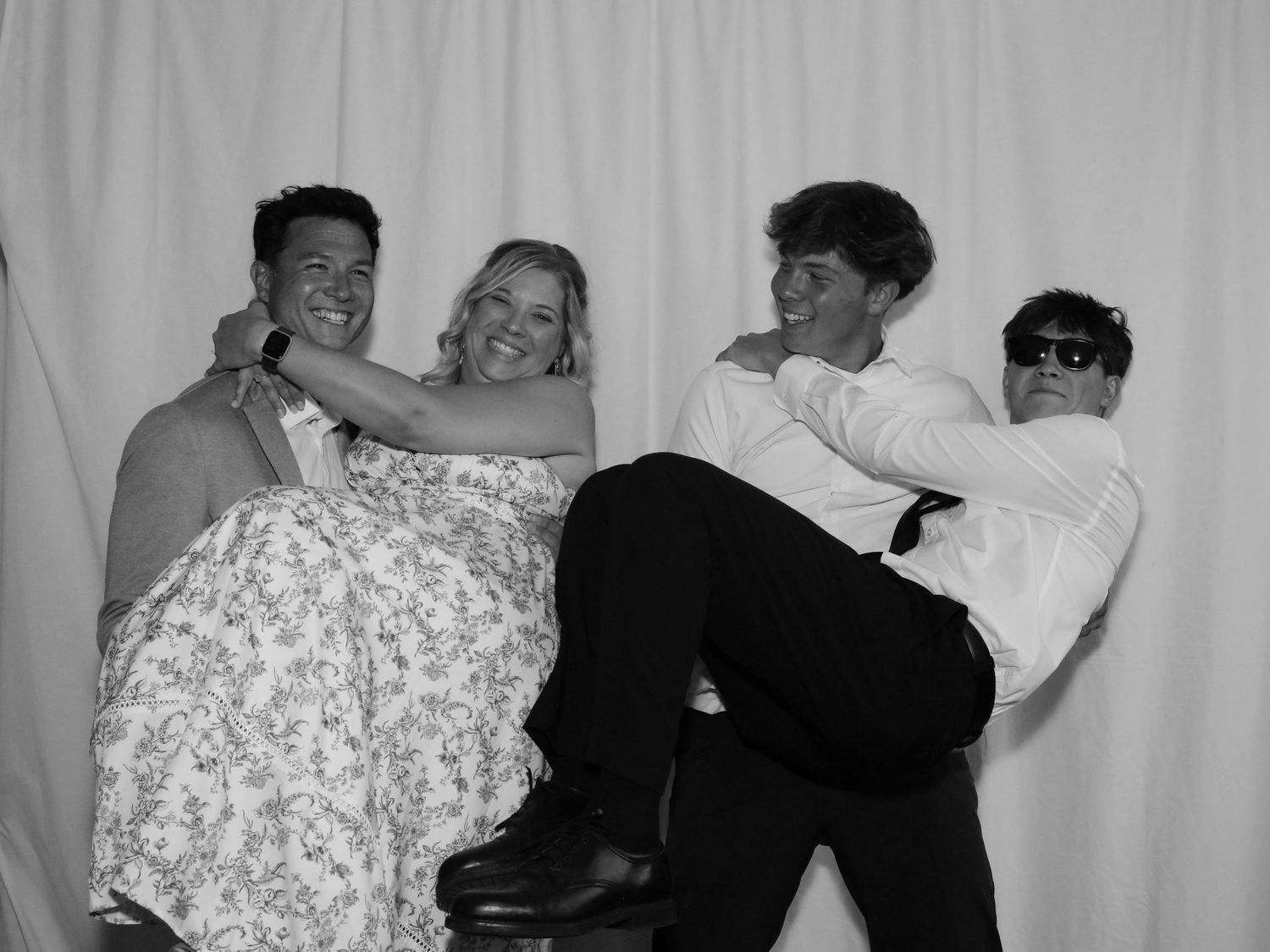 Black and white photo booth shot of four young adults laughing and posing playfully at a formal event.