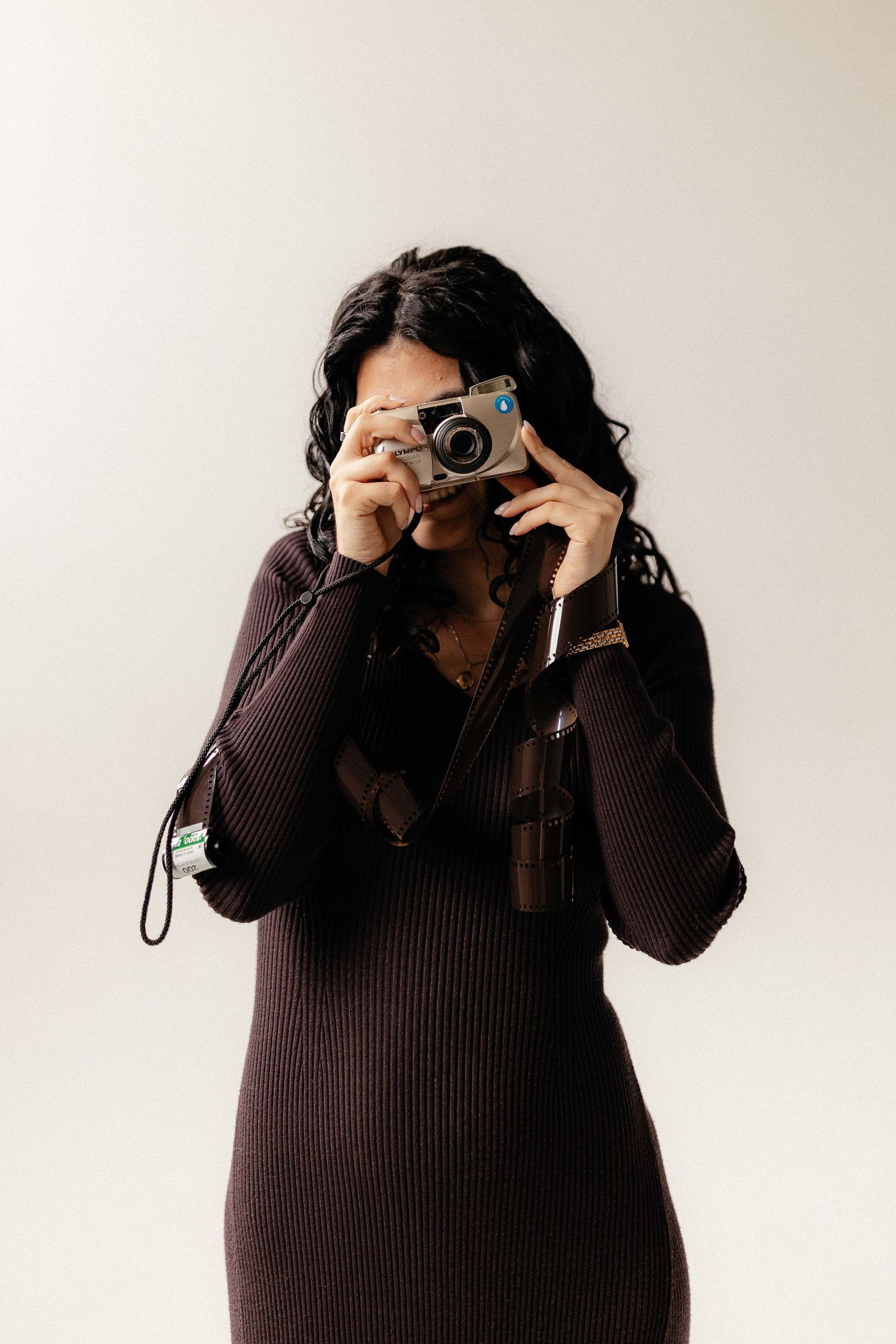 A photographer in a dark sweater takes pictures with a vintage camera against a white background.