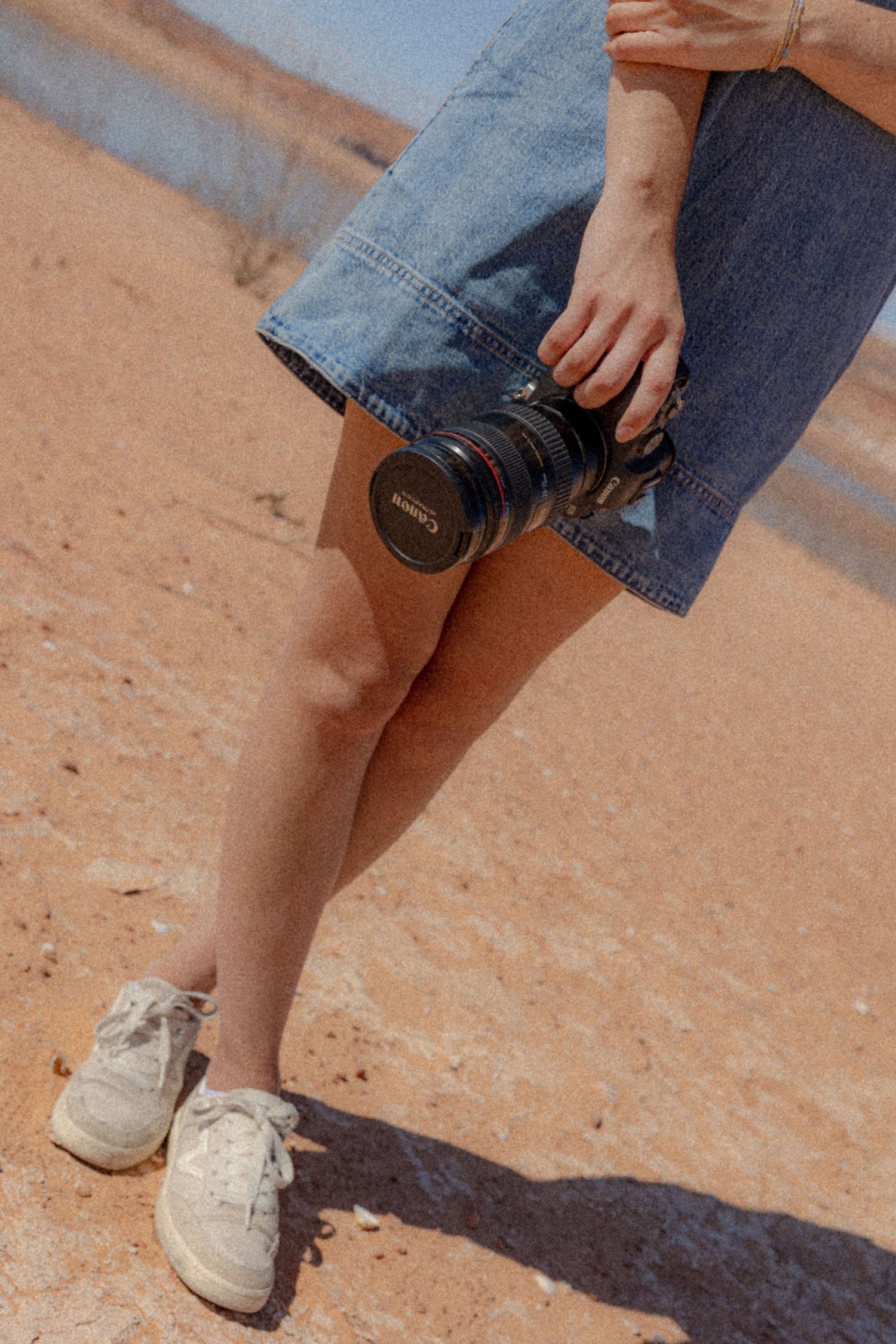 Close-up view of feet and camera equipment on desert sand.