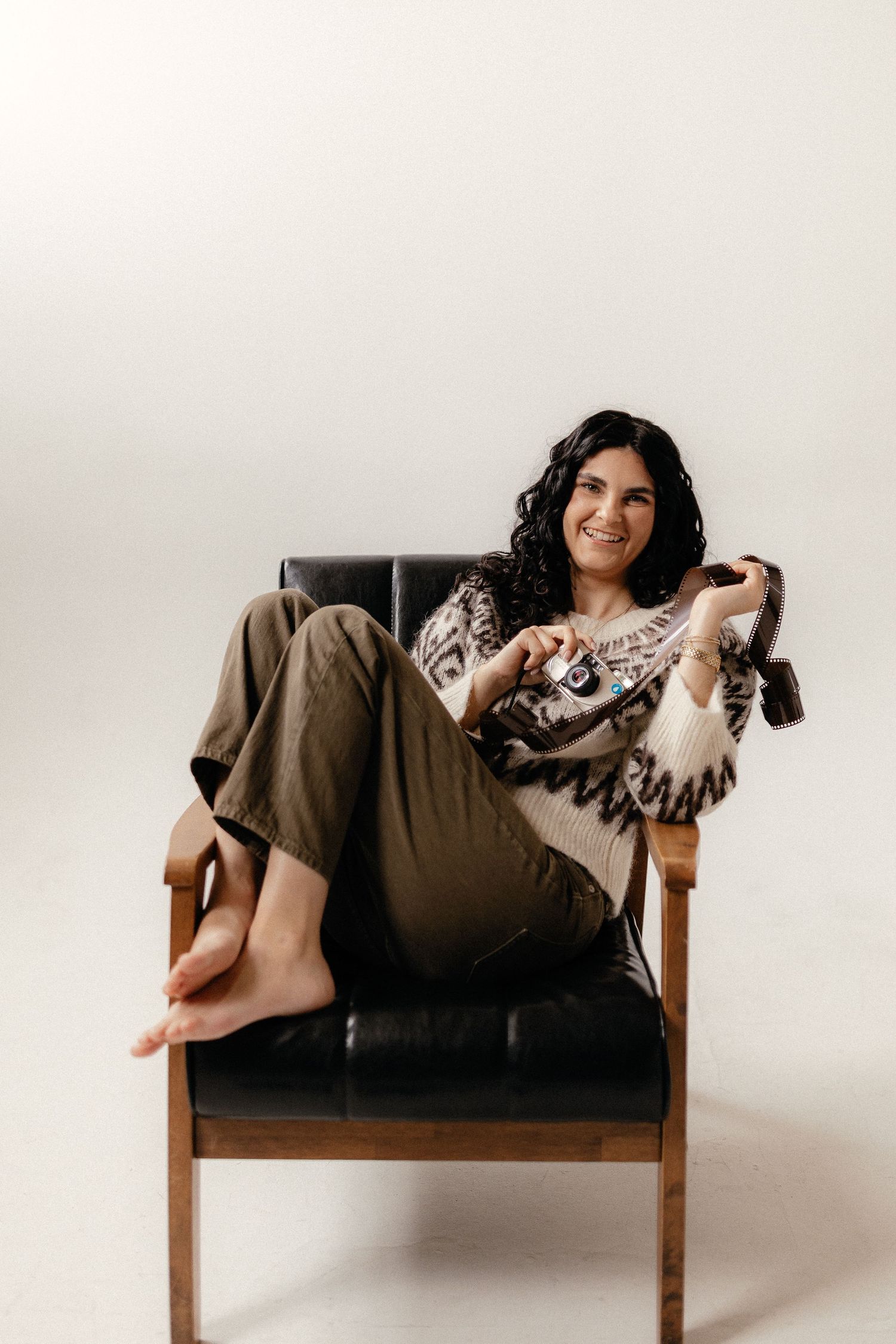 Photographer relaxes in vintage leather chair wearing casual attire.