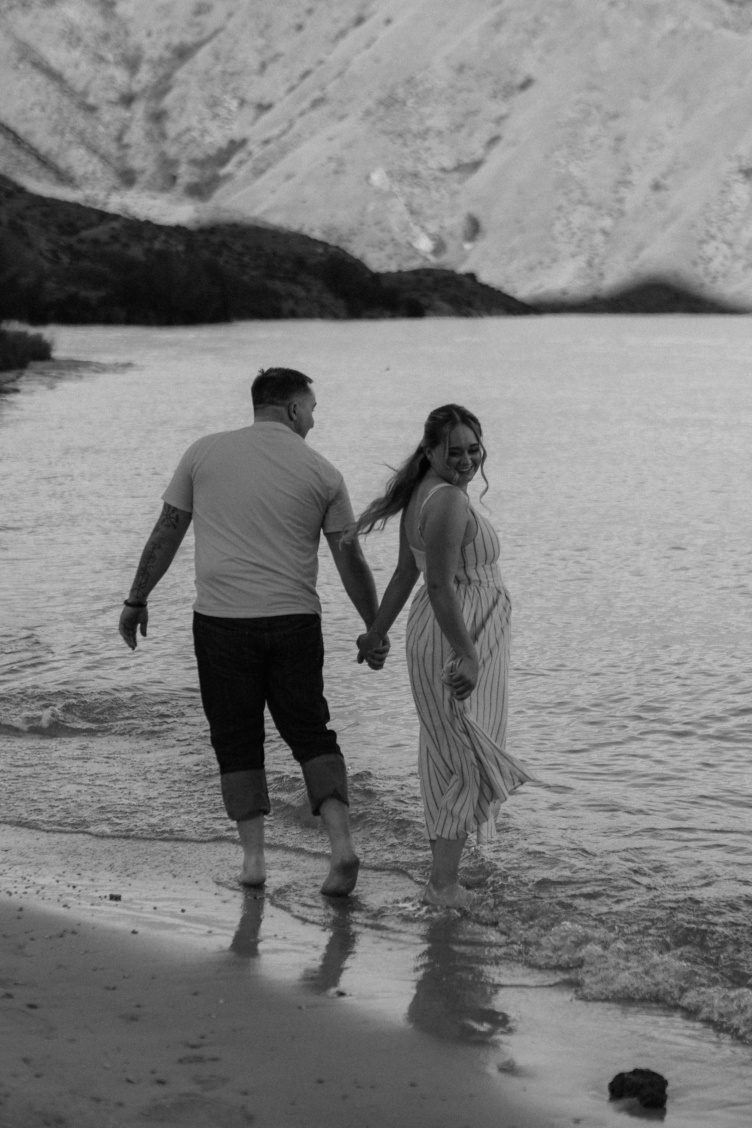Couple walking hand in hand along the shoreline in black and white.