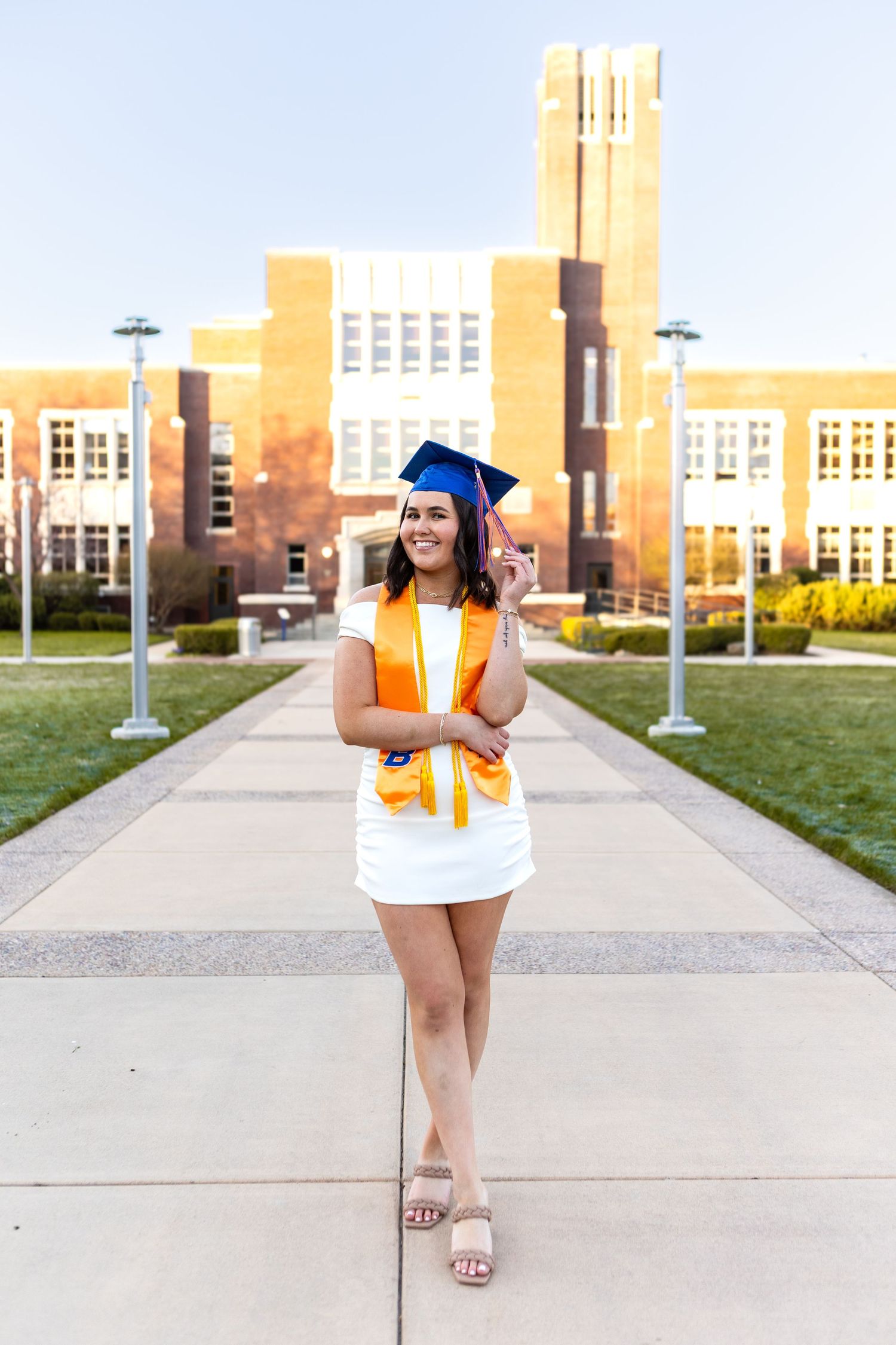 Graduate walks confidently in blue cap and gown outside historic university building.