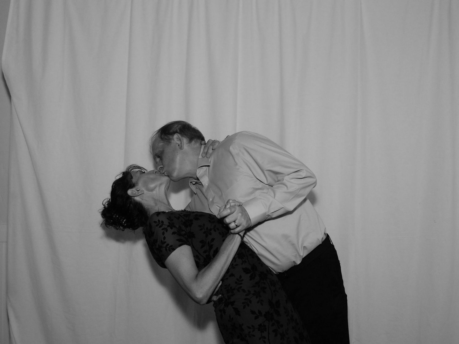 Black and white photo of a couple sharing a romantic dip kiss in front of a white backdrop.