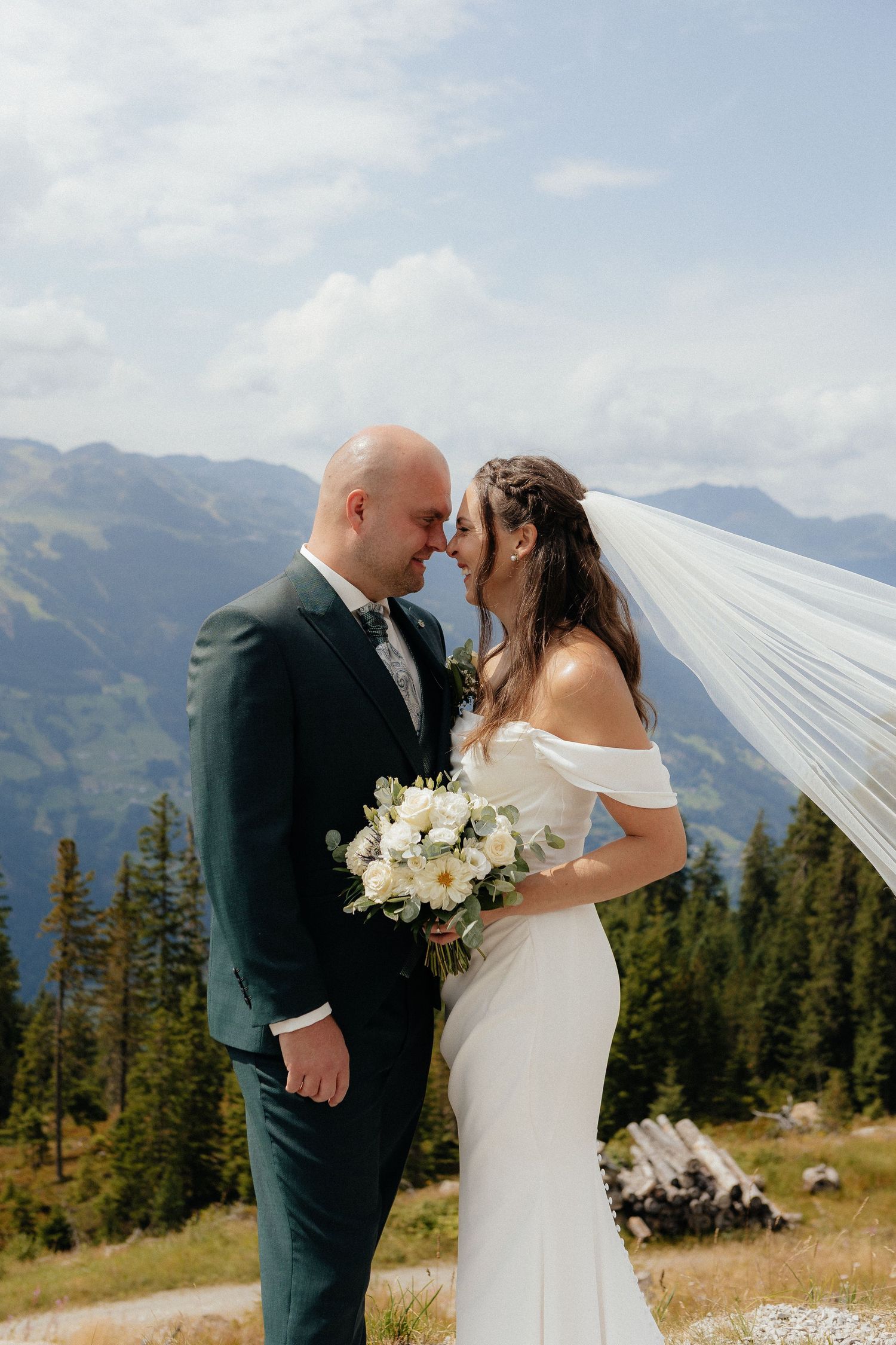 A couple shares their first kiss as newlyweds with mountain peaks in the background.