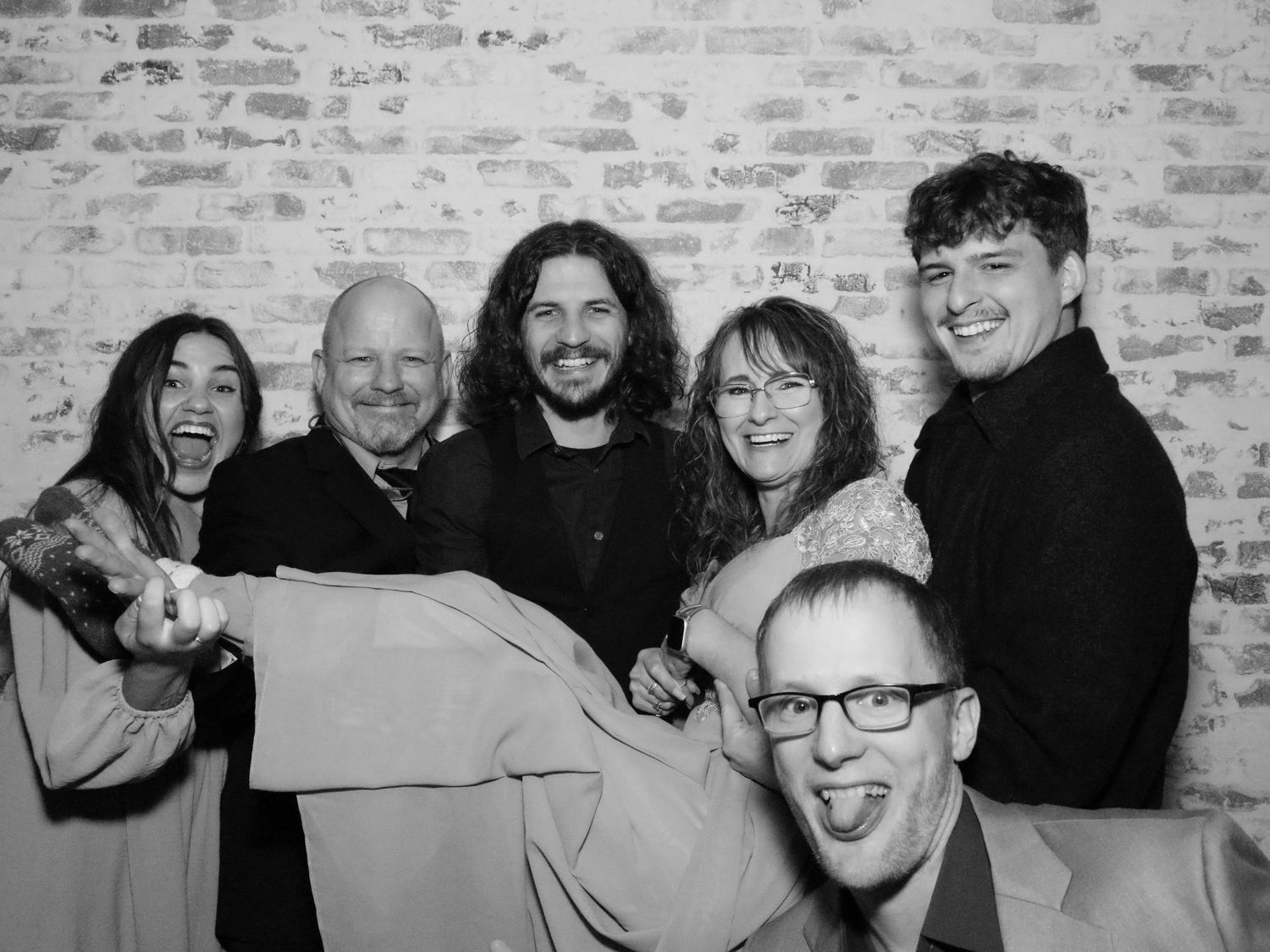 Group photo showing people laughing and making silly expressions against brick wall.
