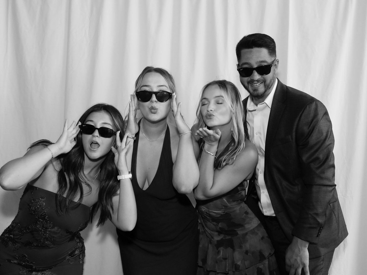 Four friends pose playfully in a black and white photo booth shot at a formal event.