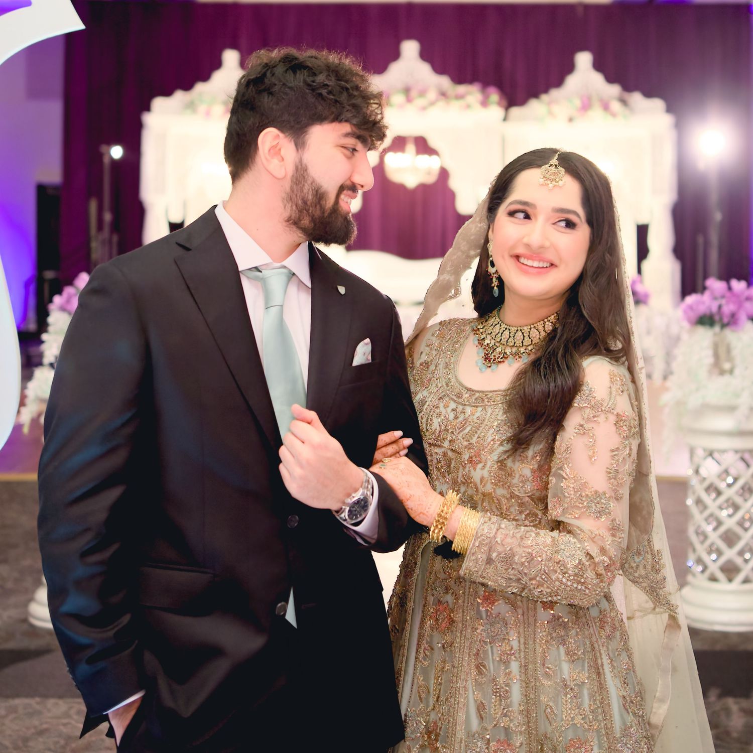 Elegant couple dancing at their reception under ornate white decorations and purple lighting.