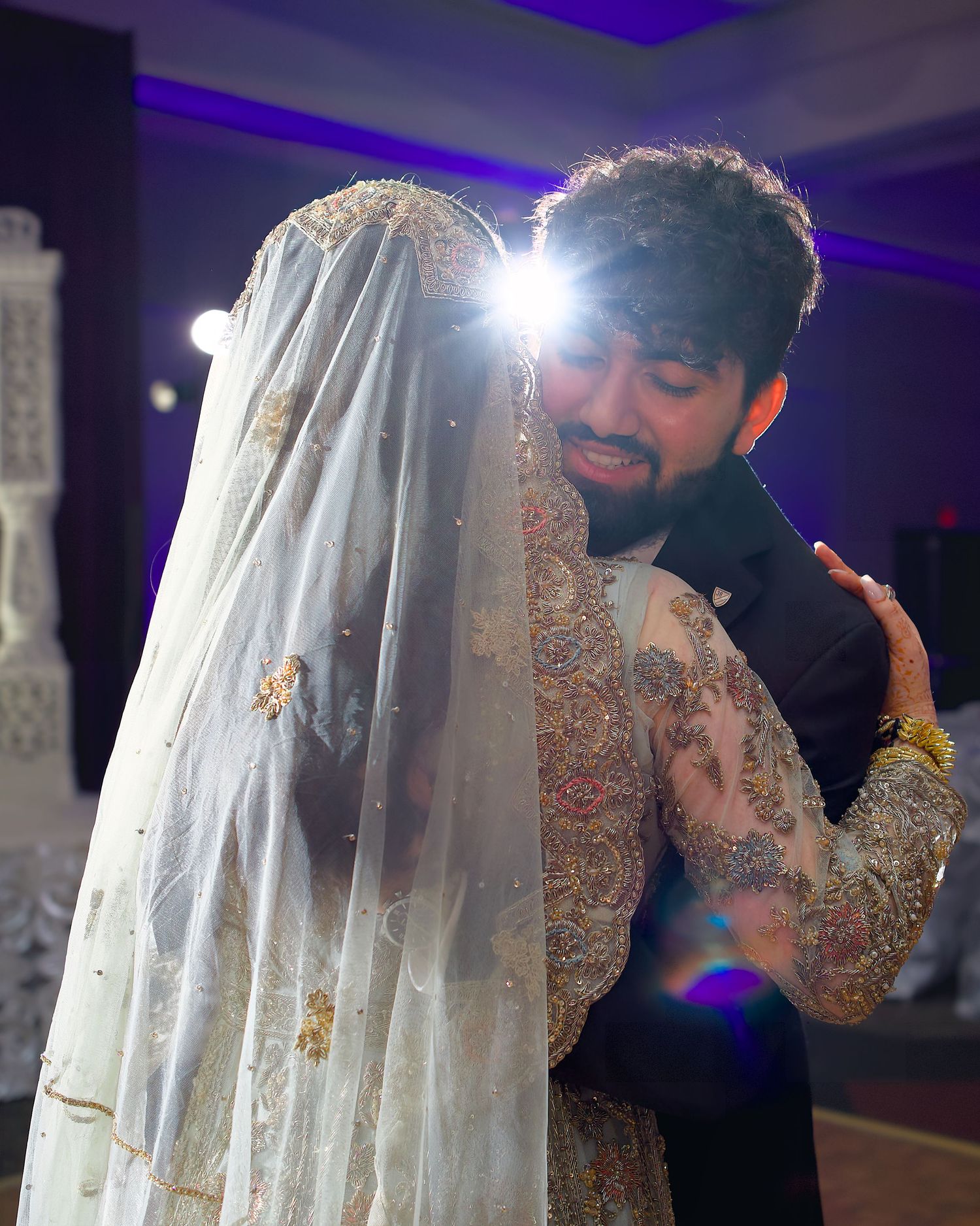 A couple shares a tender moment during a wedding celebration with purple lighting and decorative details.