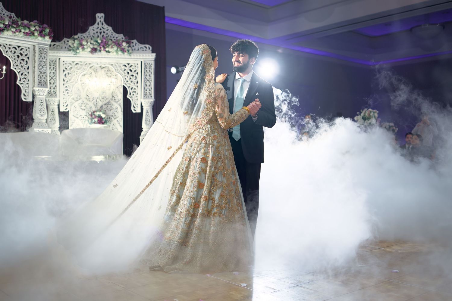 Elegant ballgown wedding dress with lace details twirls in atmospheric fog on a dance floor with purple lighting.