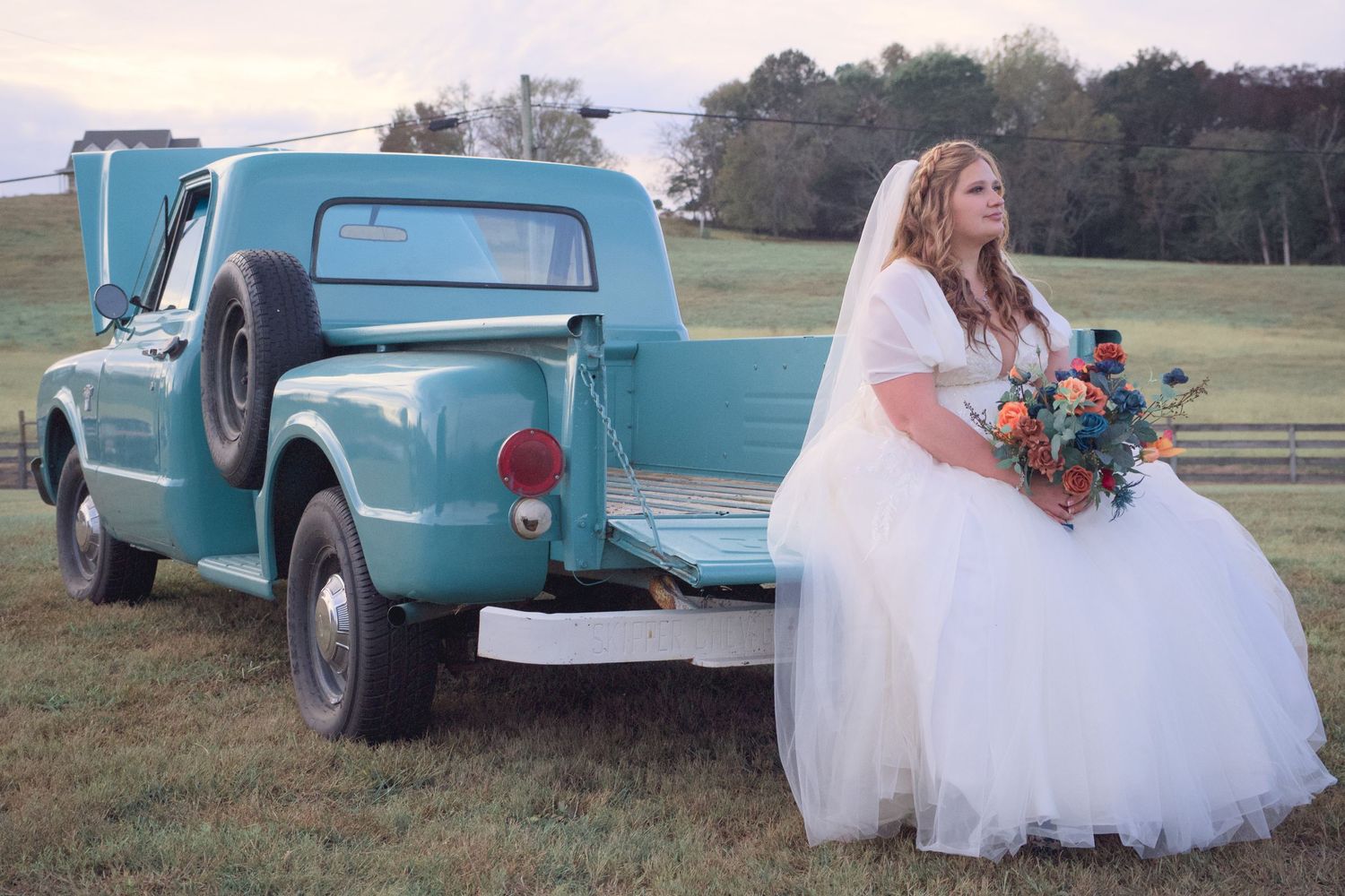 Bride in white dress poses with classic turquoise pickup truck in outdoor wedding photos.