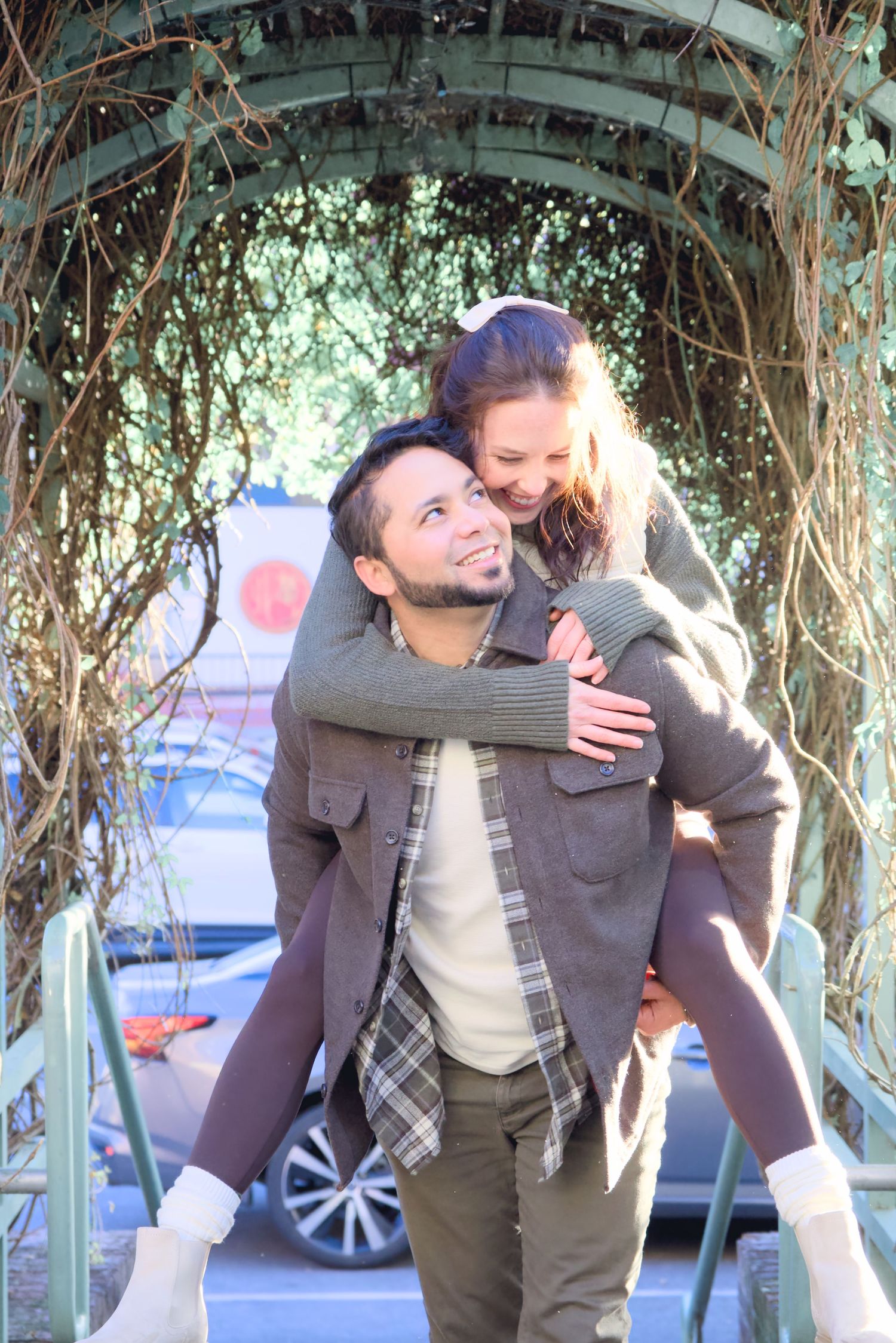 Couple enjoying a playful piggyback ride moment under a vine-covered garden arch.