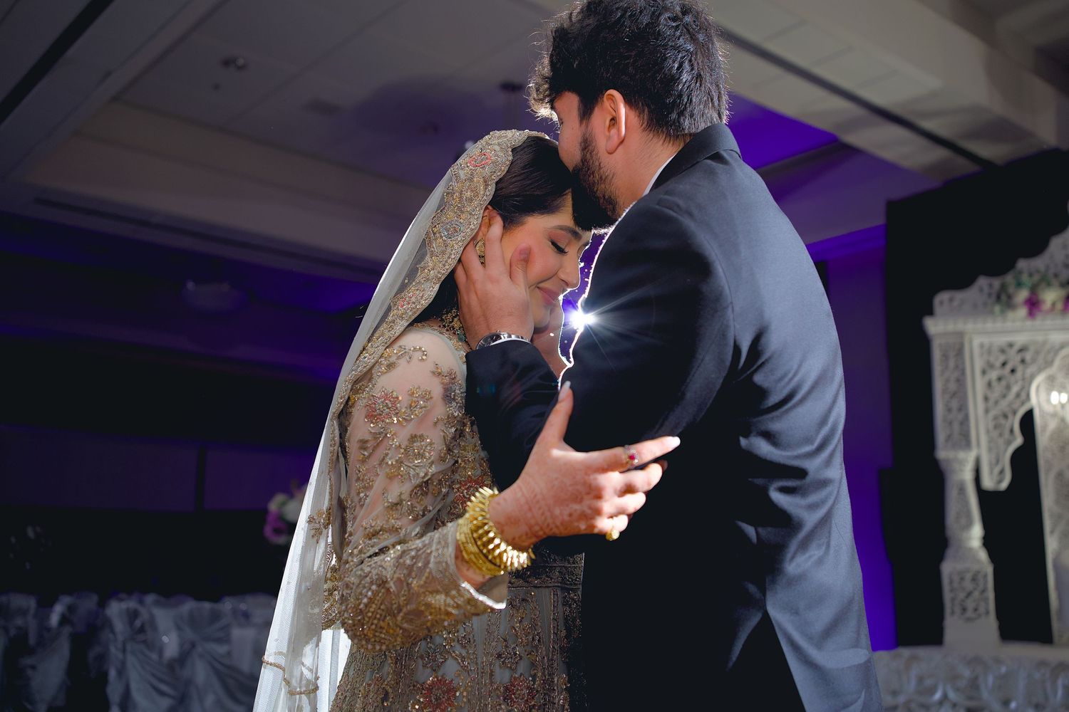 A couple shares a romantic dance together at their wedding reception under purple lighting.