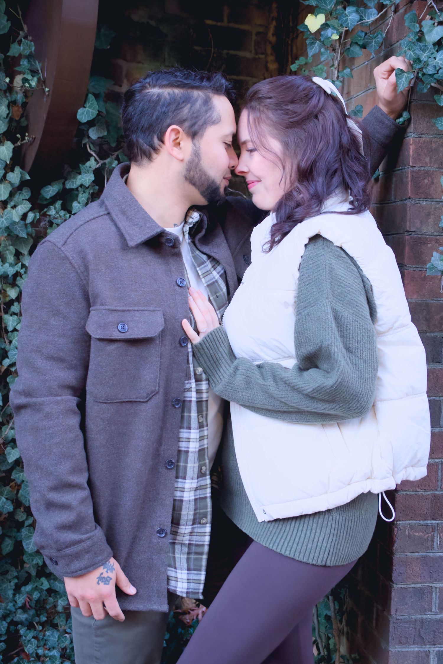 Couple shares tender moments against ivy-covered brick wall.