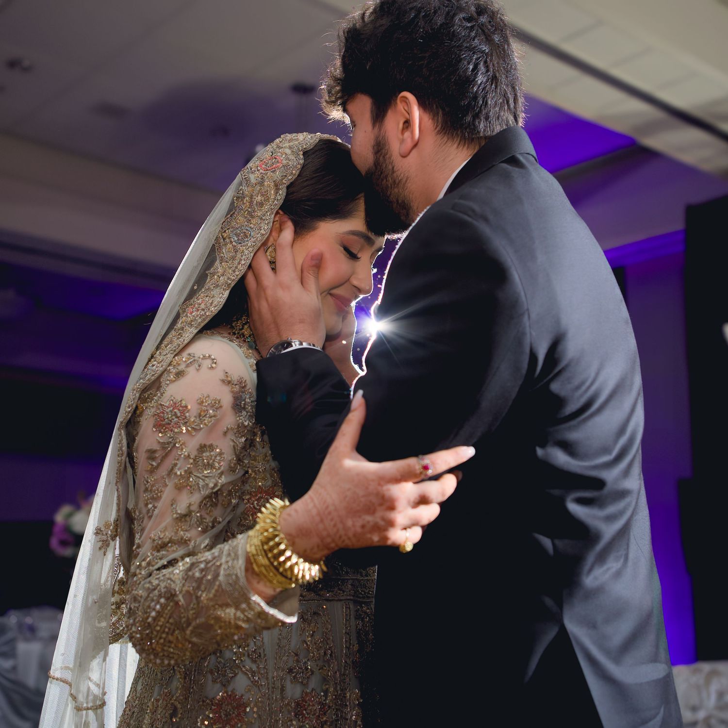 A romantic wedding couple shares intimate moments during their first dance in a purple-lit reception venue.
