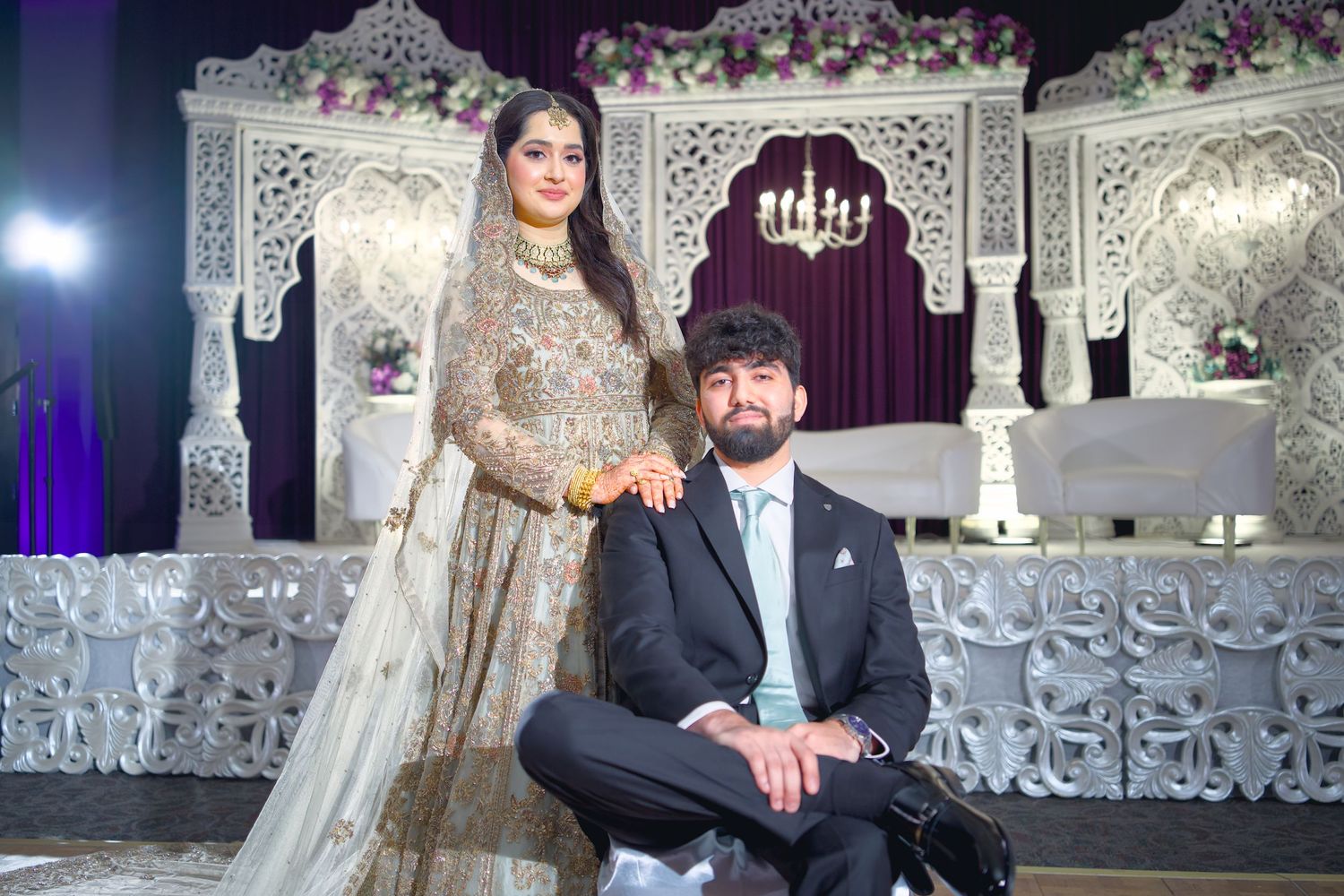 Elegant wedding reception setup with ornate white backdrop, purple lighting and formal attire.