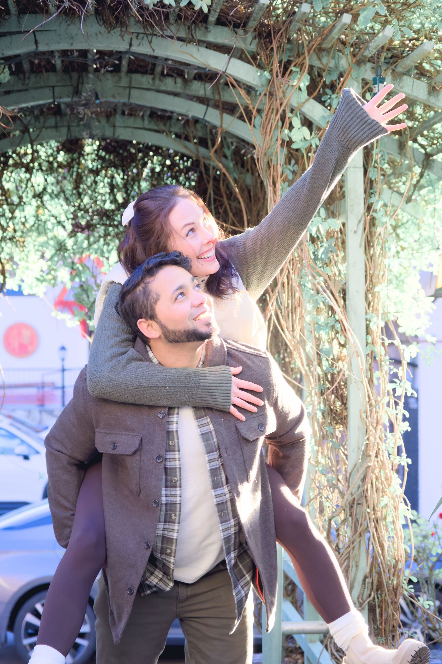 Couple having fun with piggyback ride under an ivy-covered archway.