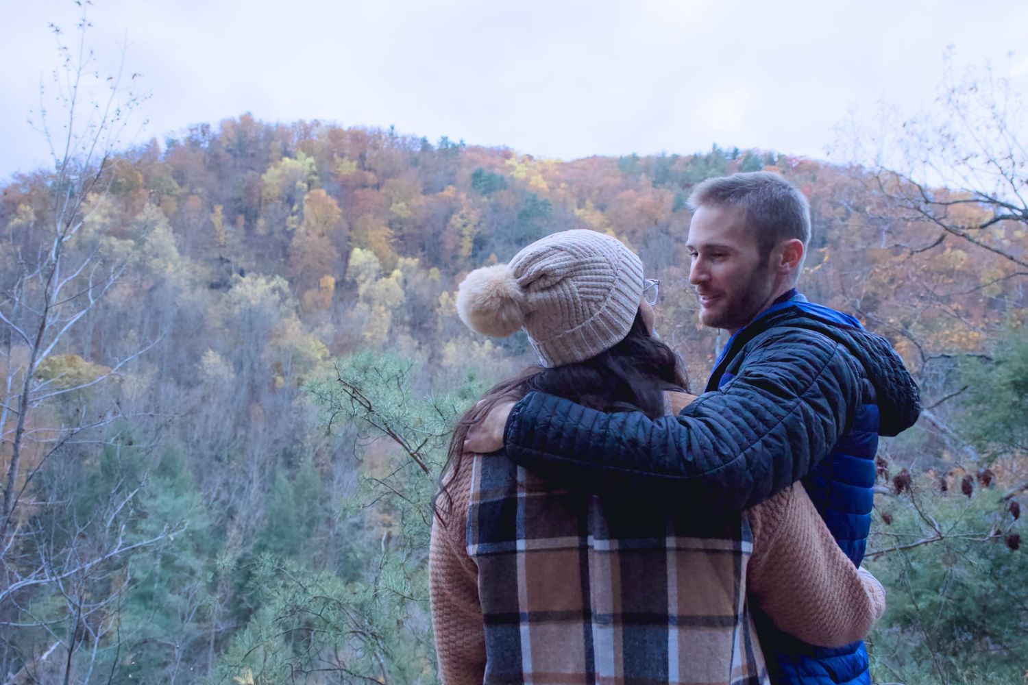 Couple embraces during an autumn photoshoot with colorful fall foliage in the background.