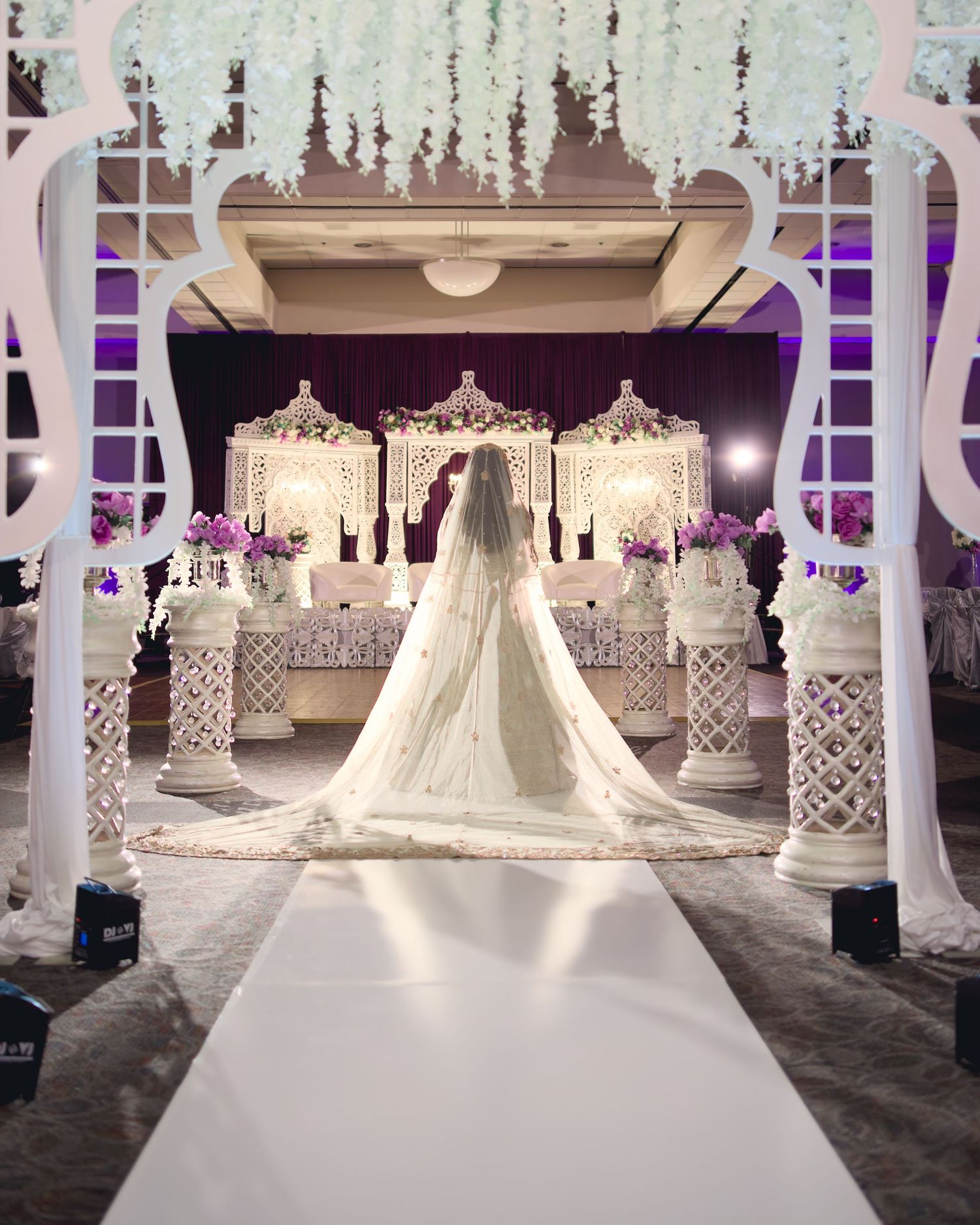 Elegant wedding venue display featuring ornate white decor, columns and dramatic purple lighting.