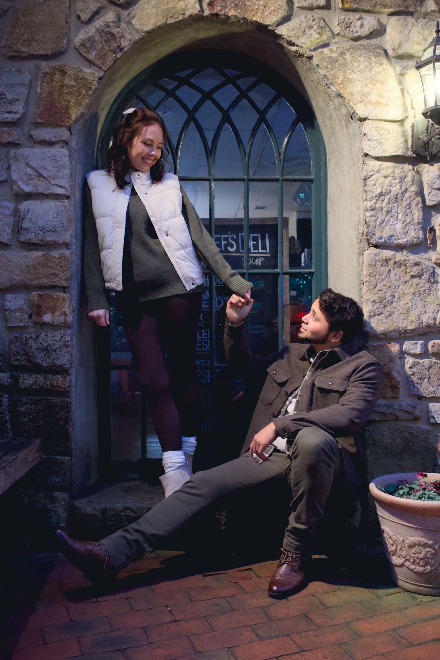 A couple poses playfully by stone archways and brick walls.