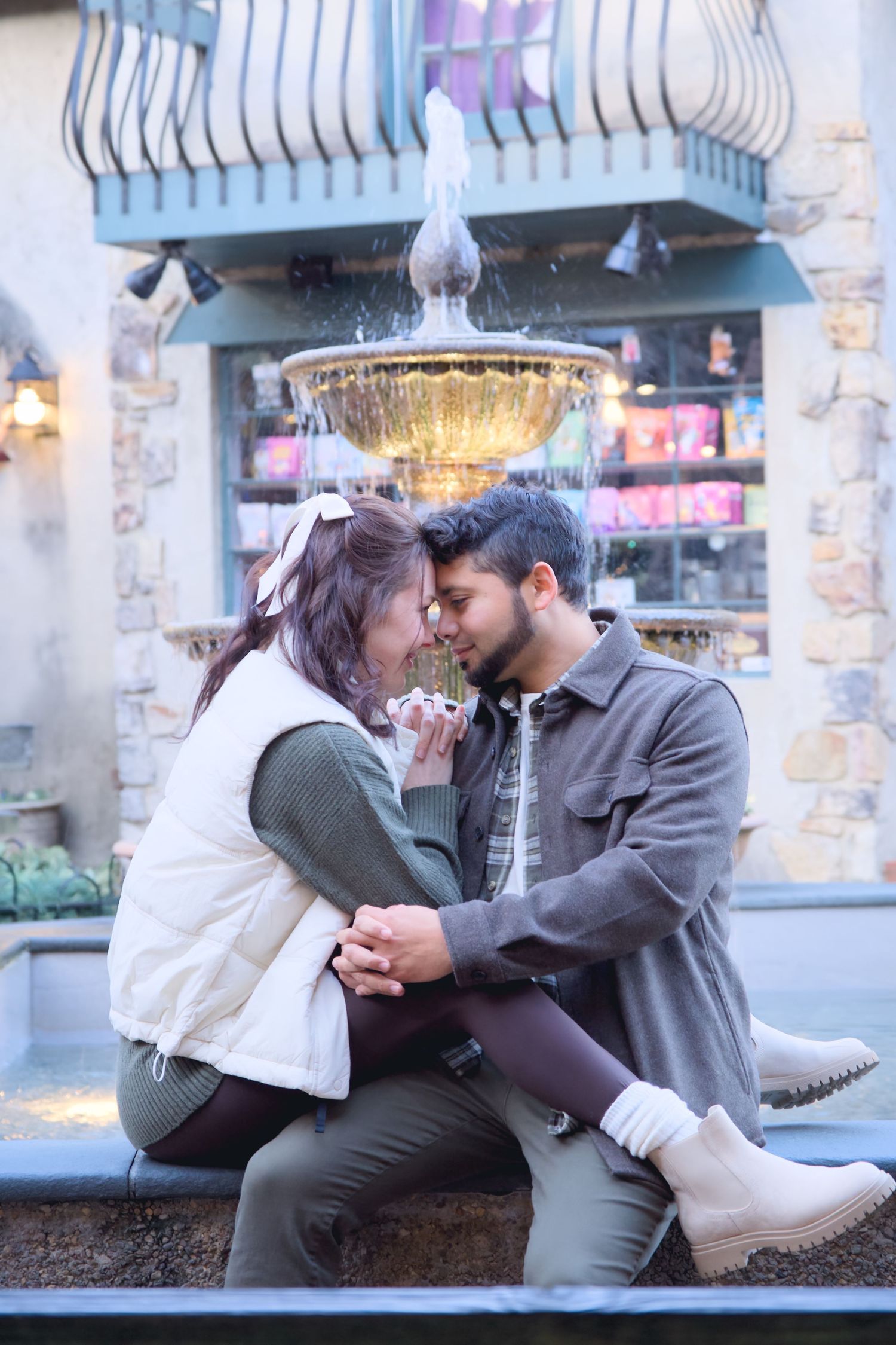 Couple shares romantic moments on a bench during an urban photoshoot with city lights in background.