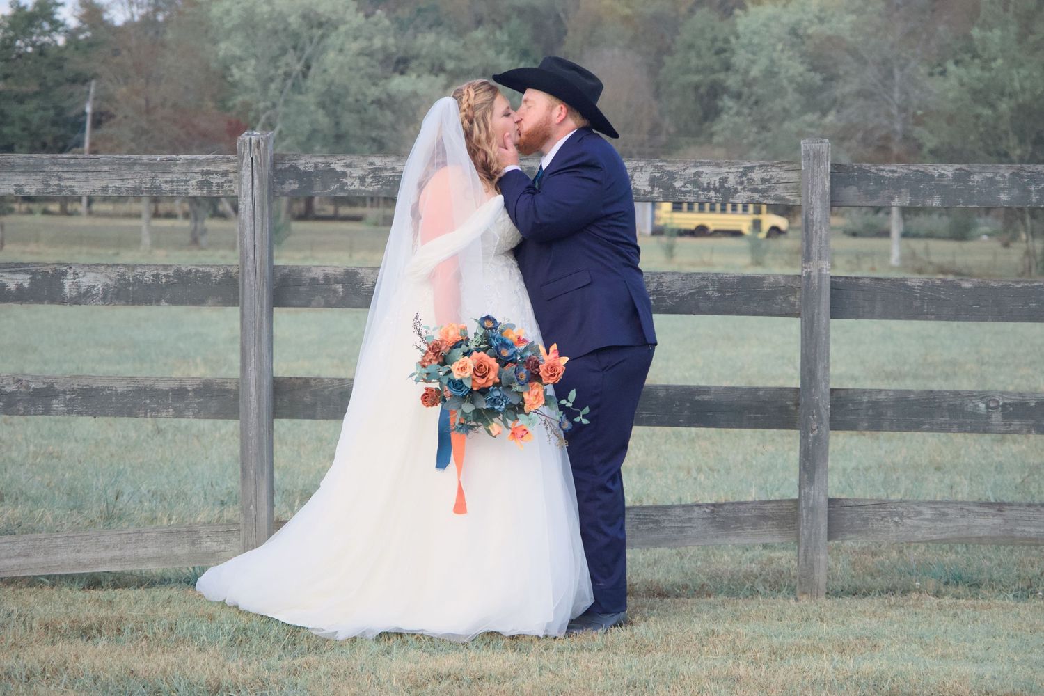 Romantic couple poses for wedding photos along a rustic wooden fence in an outdoor setting.