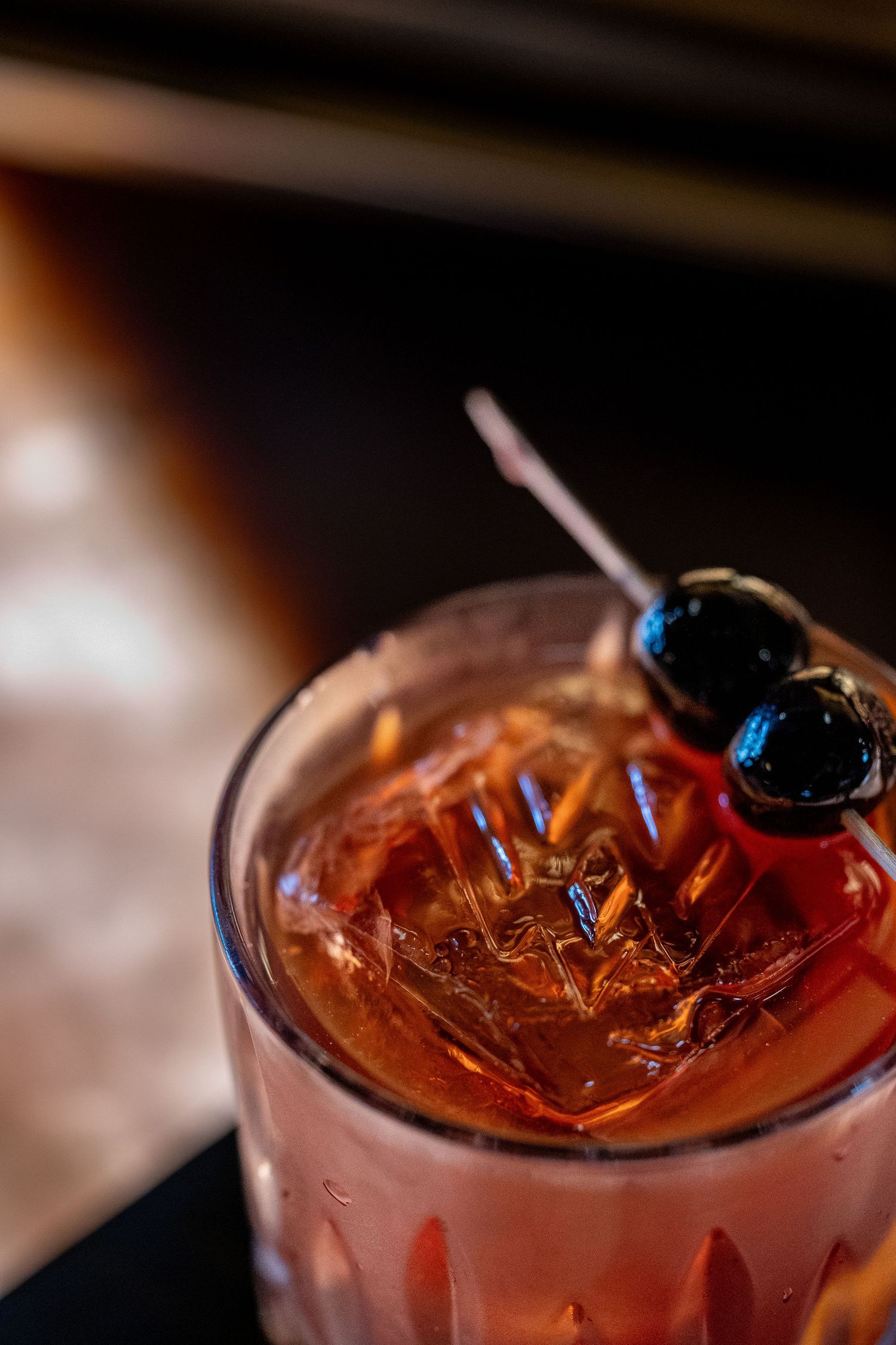 Macro shots of a red cocktail garnished with dark berries and ice.