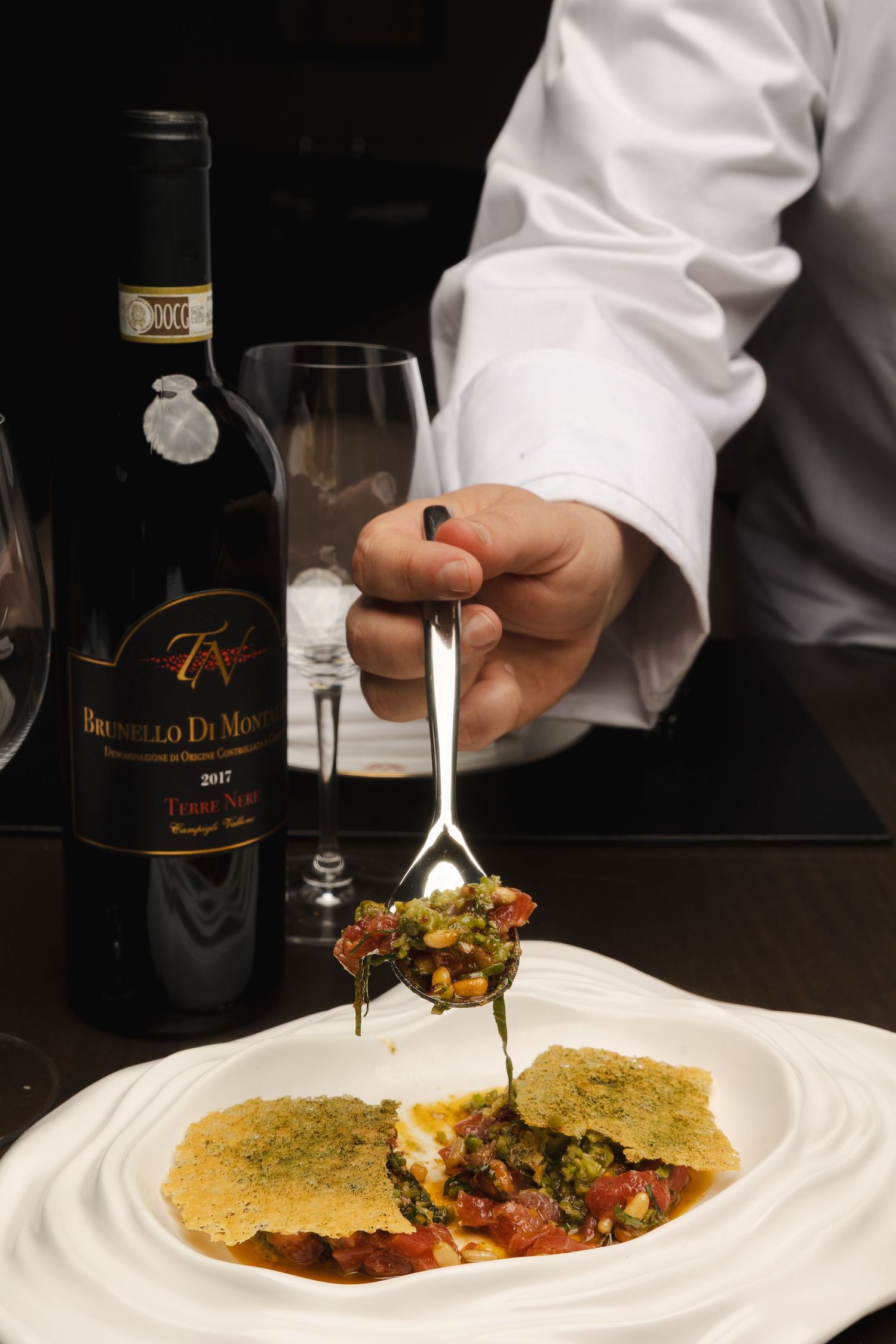 Chef plating an elegant dish with precision using culinary tweezers in a fine dining setting.