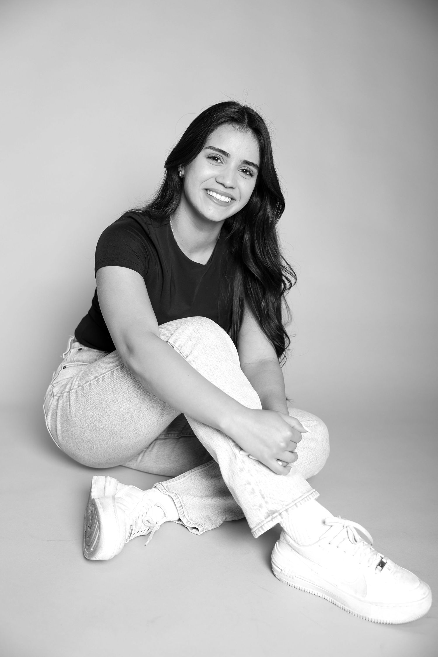 Black and white portrait of person in casual wear sitting with white sneakers.
