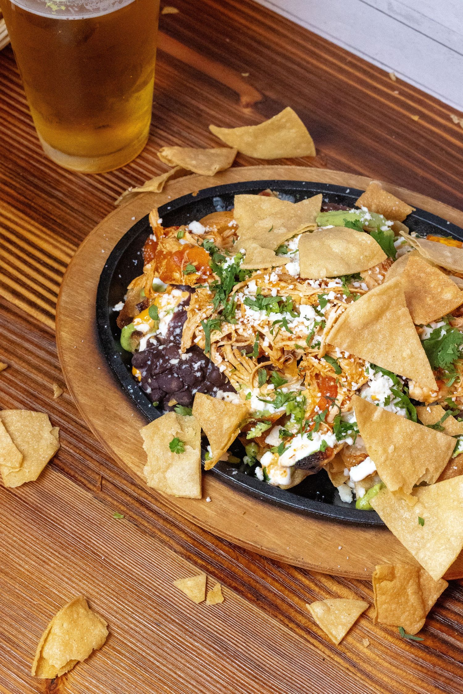 Mexican-style nachos with cheese and toppings served on wooden table with beer.