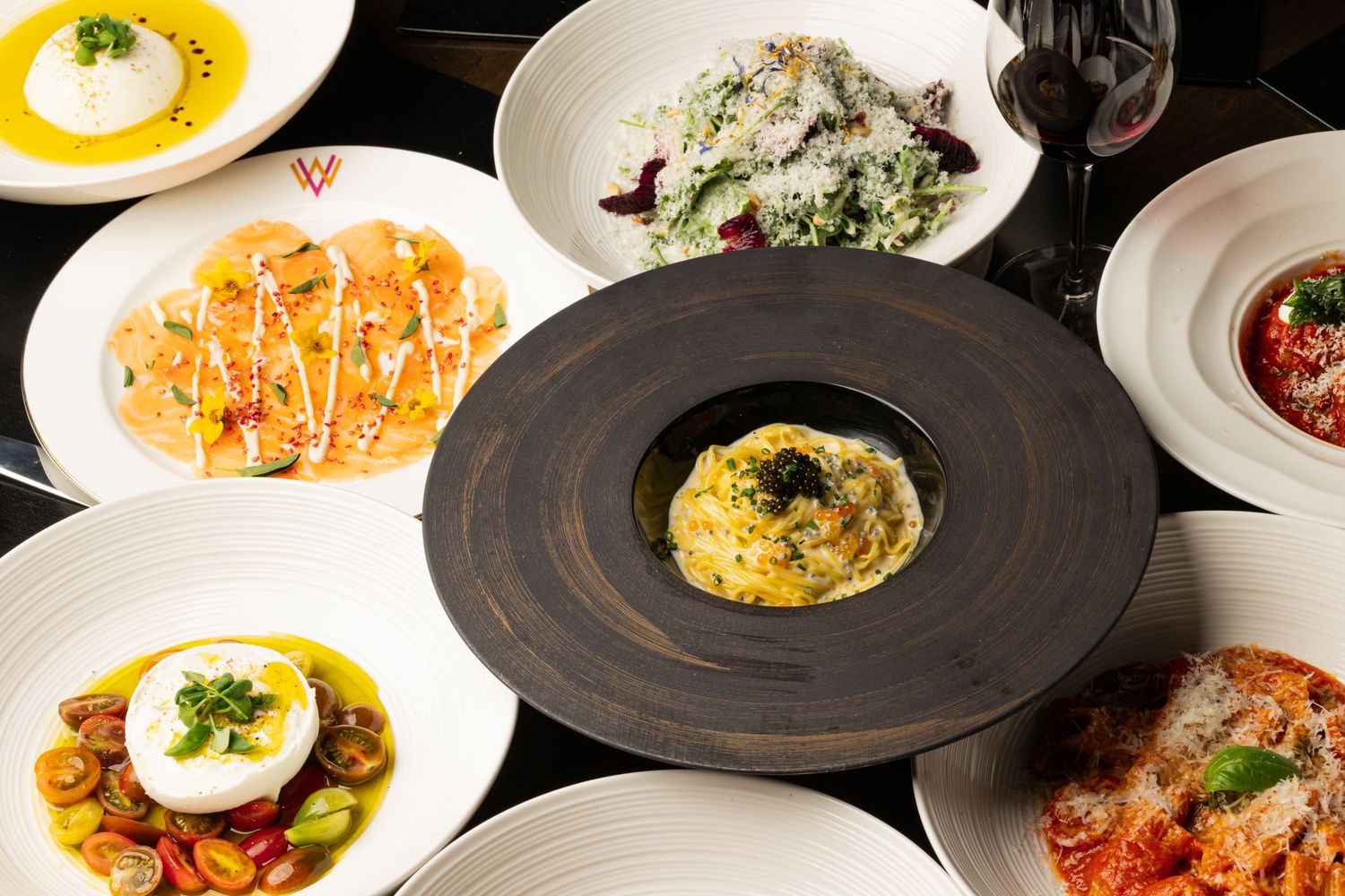 Elegant plated dishes including pasta, seafood, and sauces arranged on dark plates at an upscale restaurant.