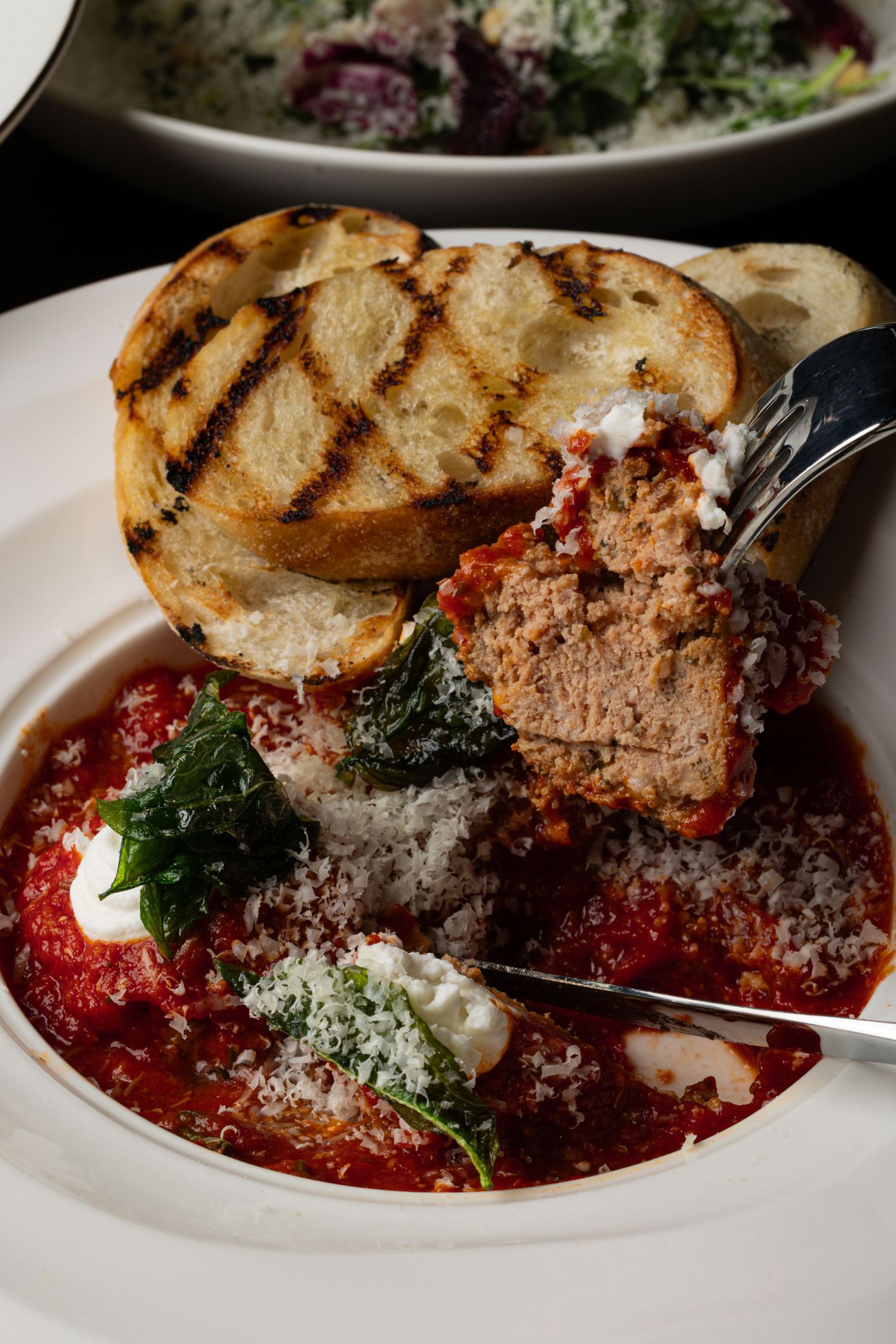 Italian meatballs in rich tomato sauce with melted cheese and grilled bread on a white plate.