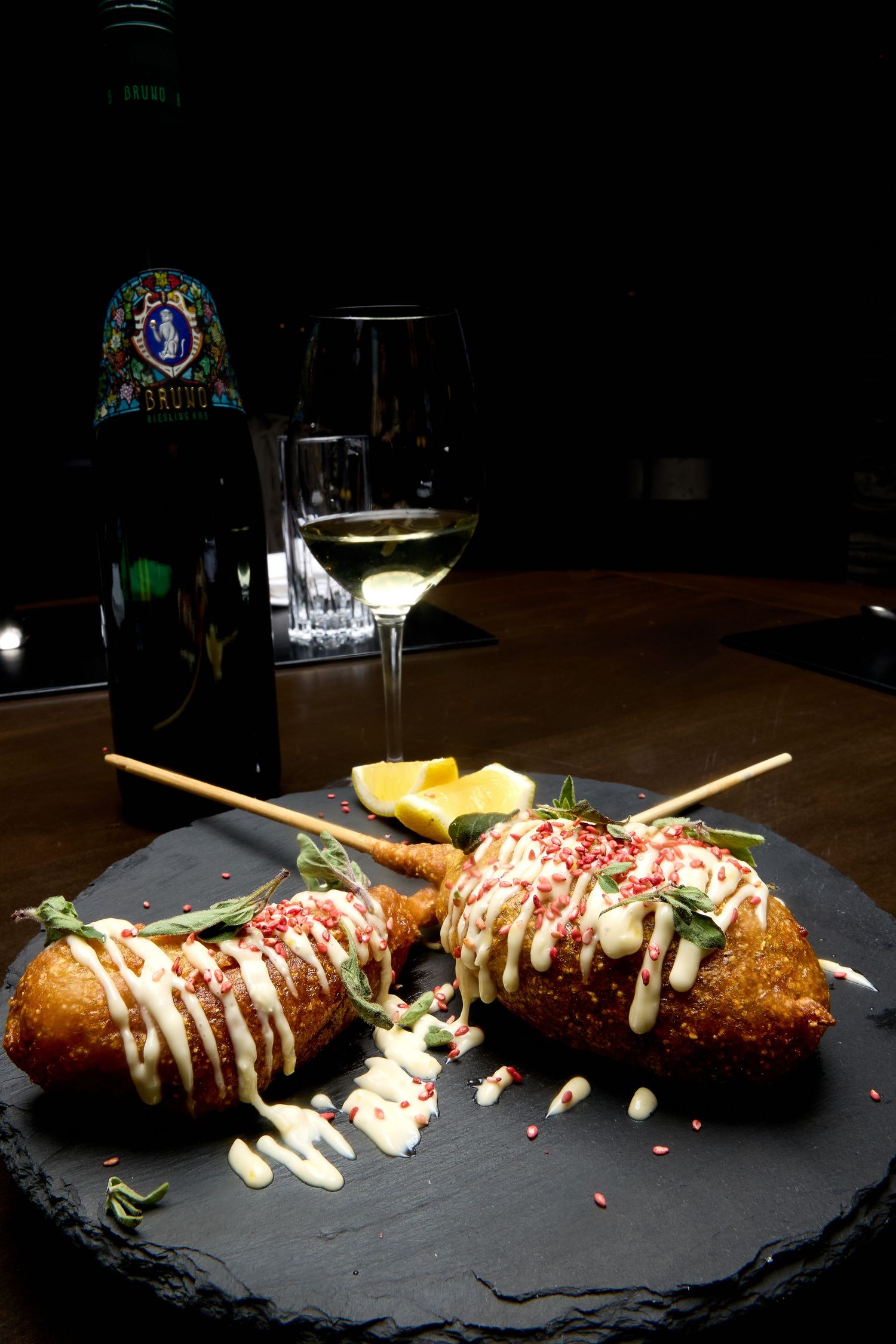 Elegant croquettes drizzled with white sauce and garnishes presented on a black slate plate.