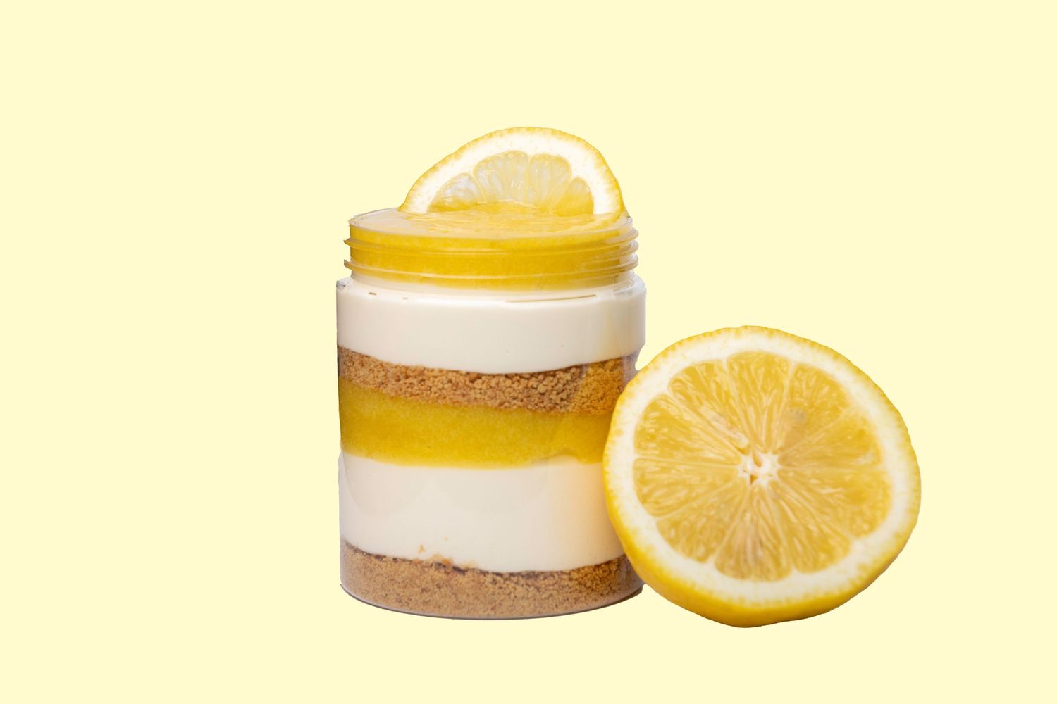 Fresh lemon slices paired with yellow beauty product jars on pale yellow background.