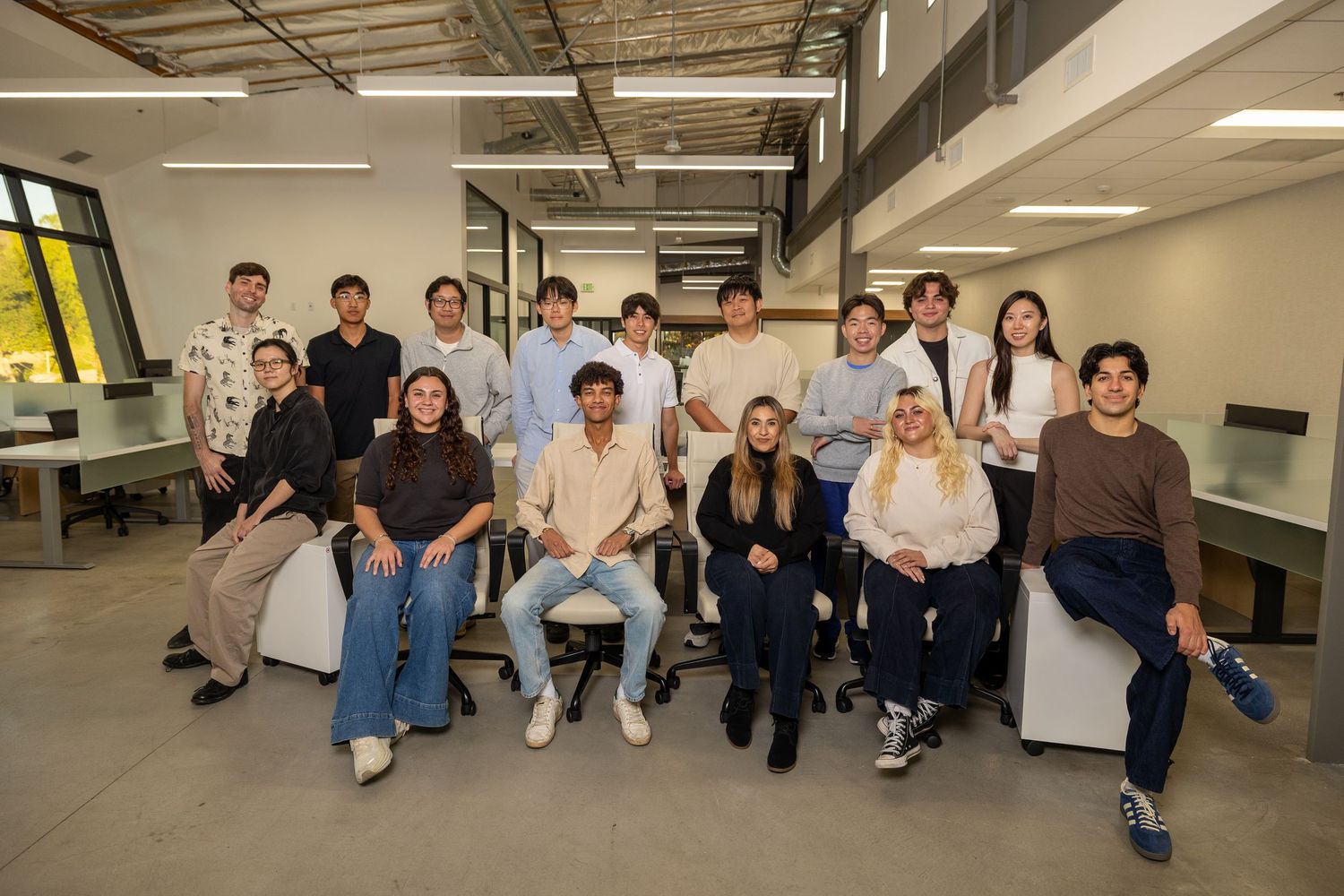Group of students sitting casually along a hallway wall in a modern building.