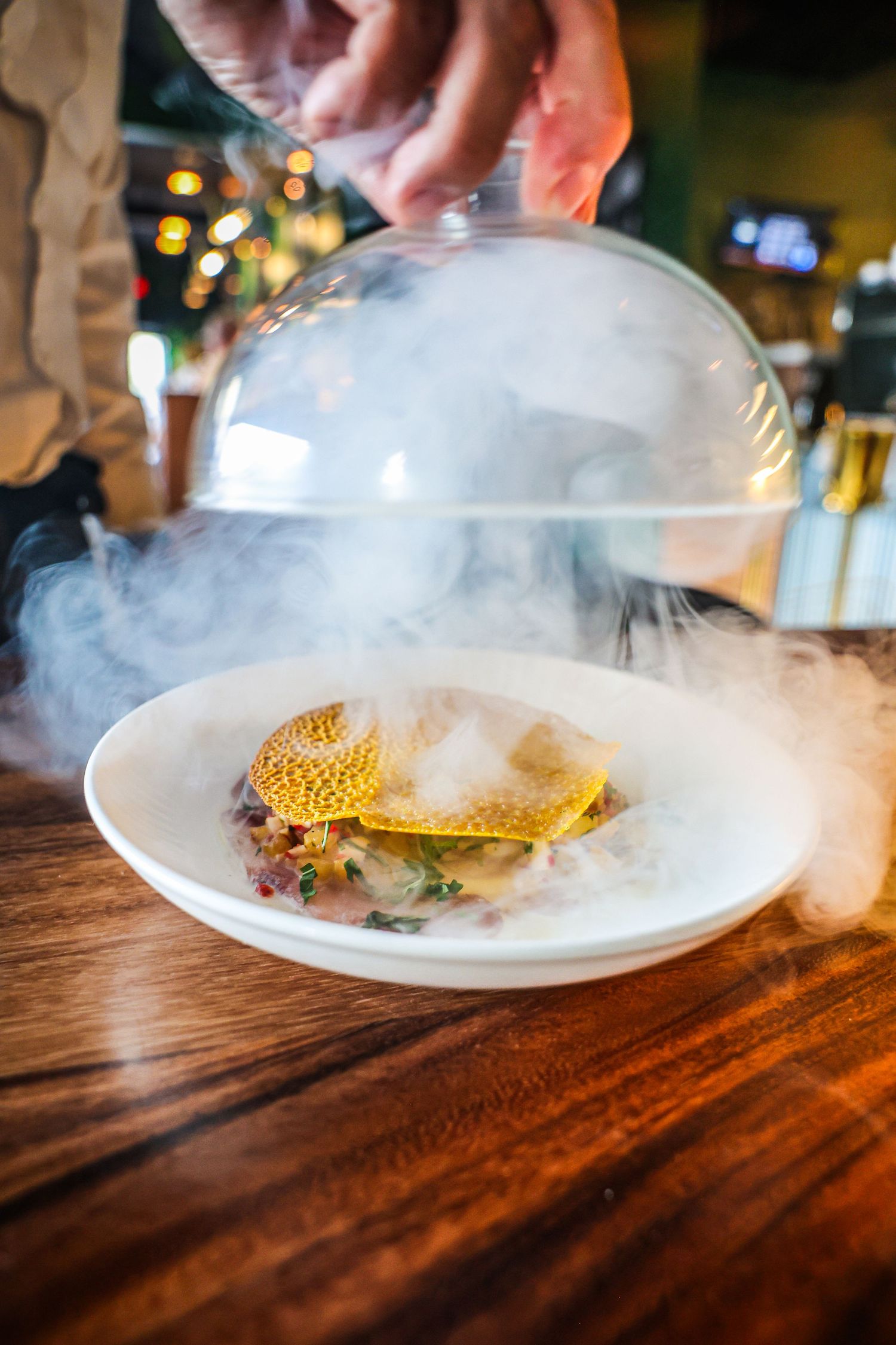 Dramatic presentation of a dish being revealed with smoke under a glass cloche.