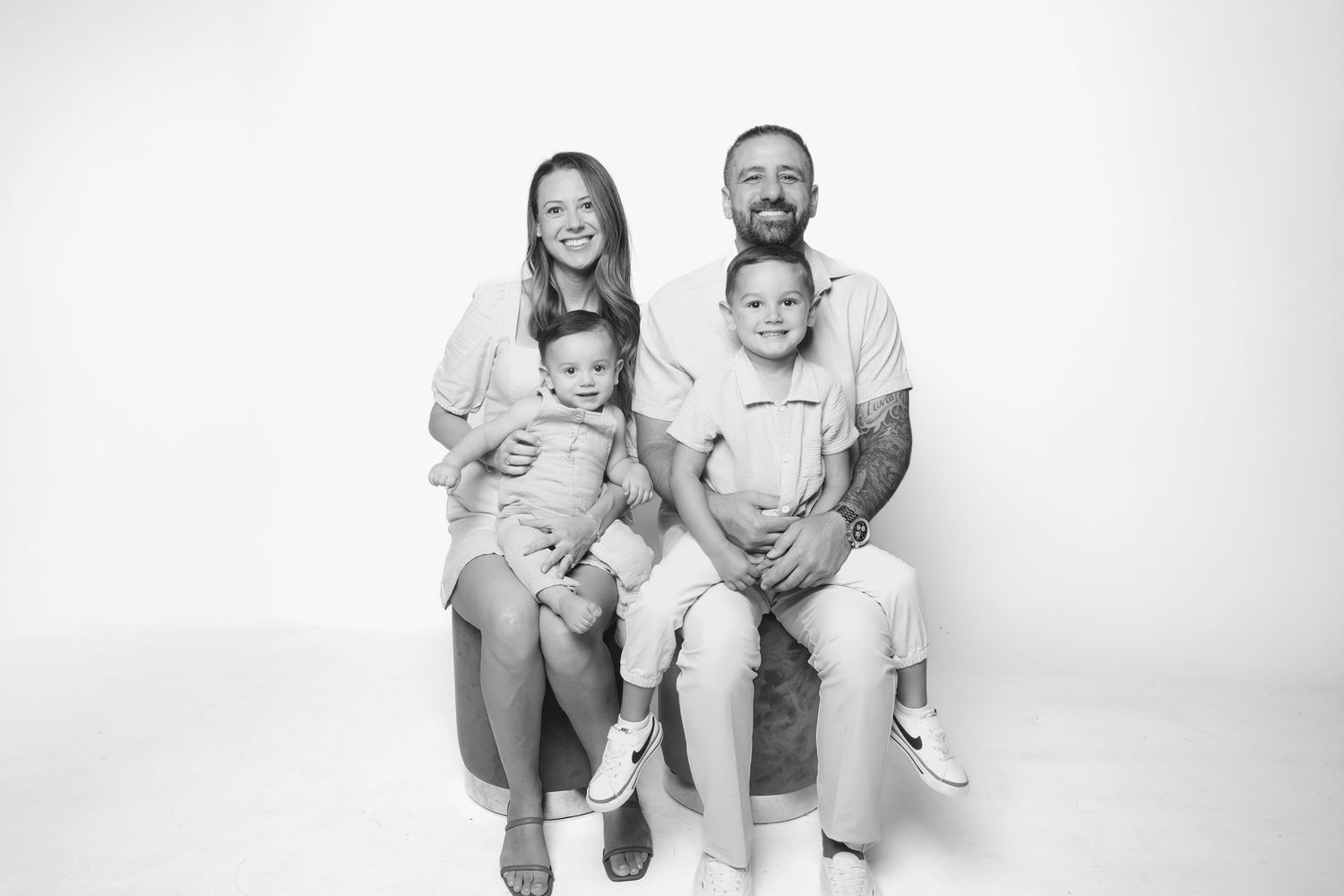 A black and white studio portrait of a family of four sitting together against a plain background.