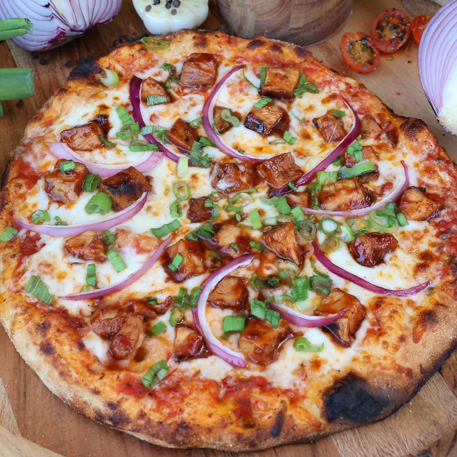 Wood-fired pizza topped with red onions, herbs, and melted cheese on a wooden serving board.