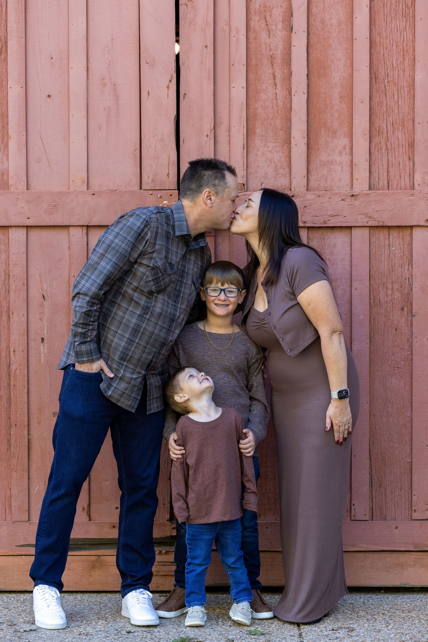 A family poses for a portrait against a rustic red wooden wall background.