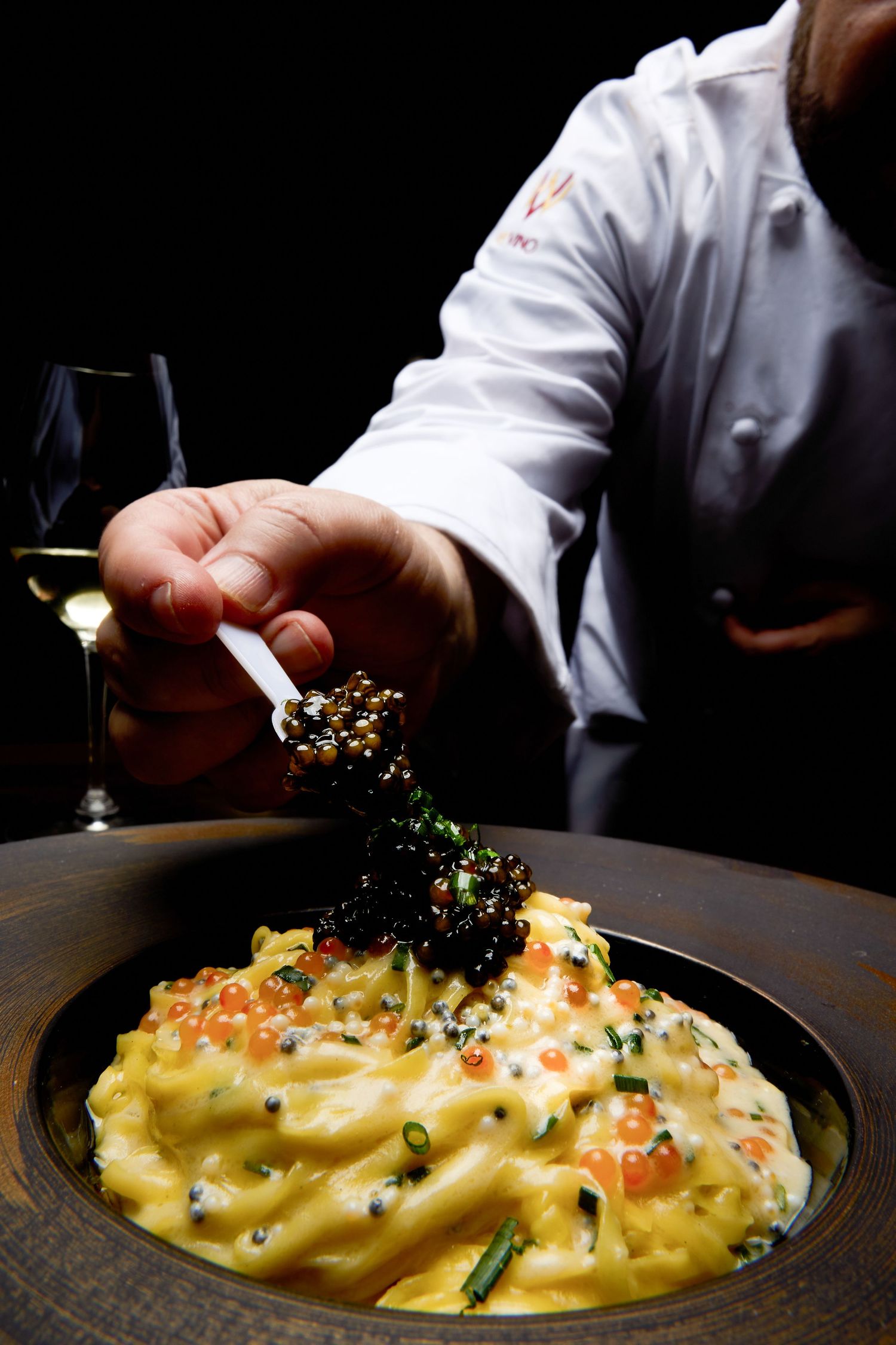 Creamy pasta dish being garnished with black caviar in a dramatic lighting setting.