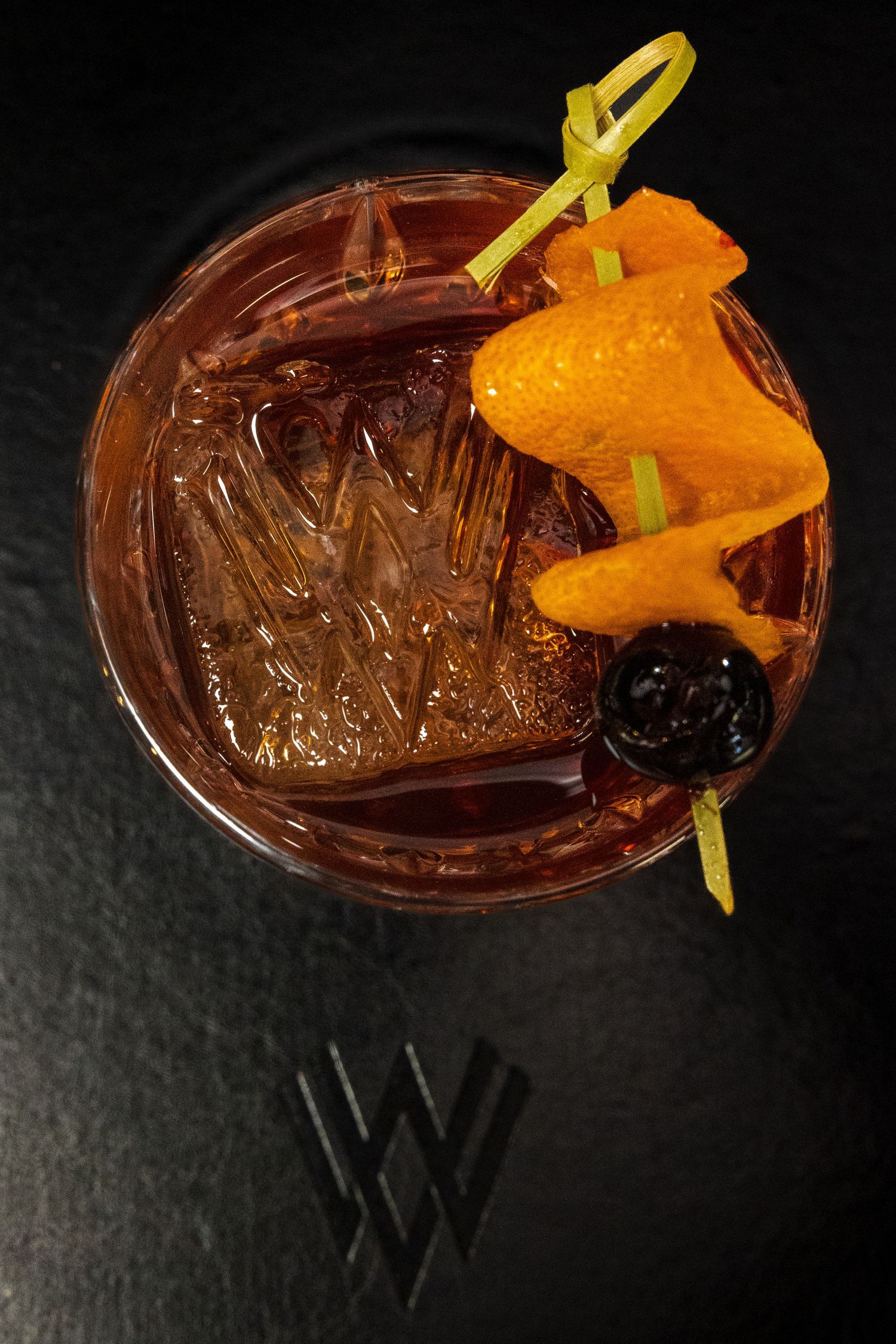 Cocktail garnished with orange slice and citrus peel on dark surface.